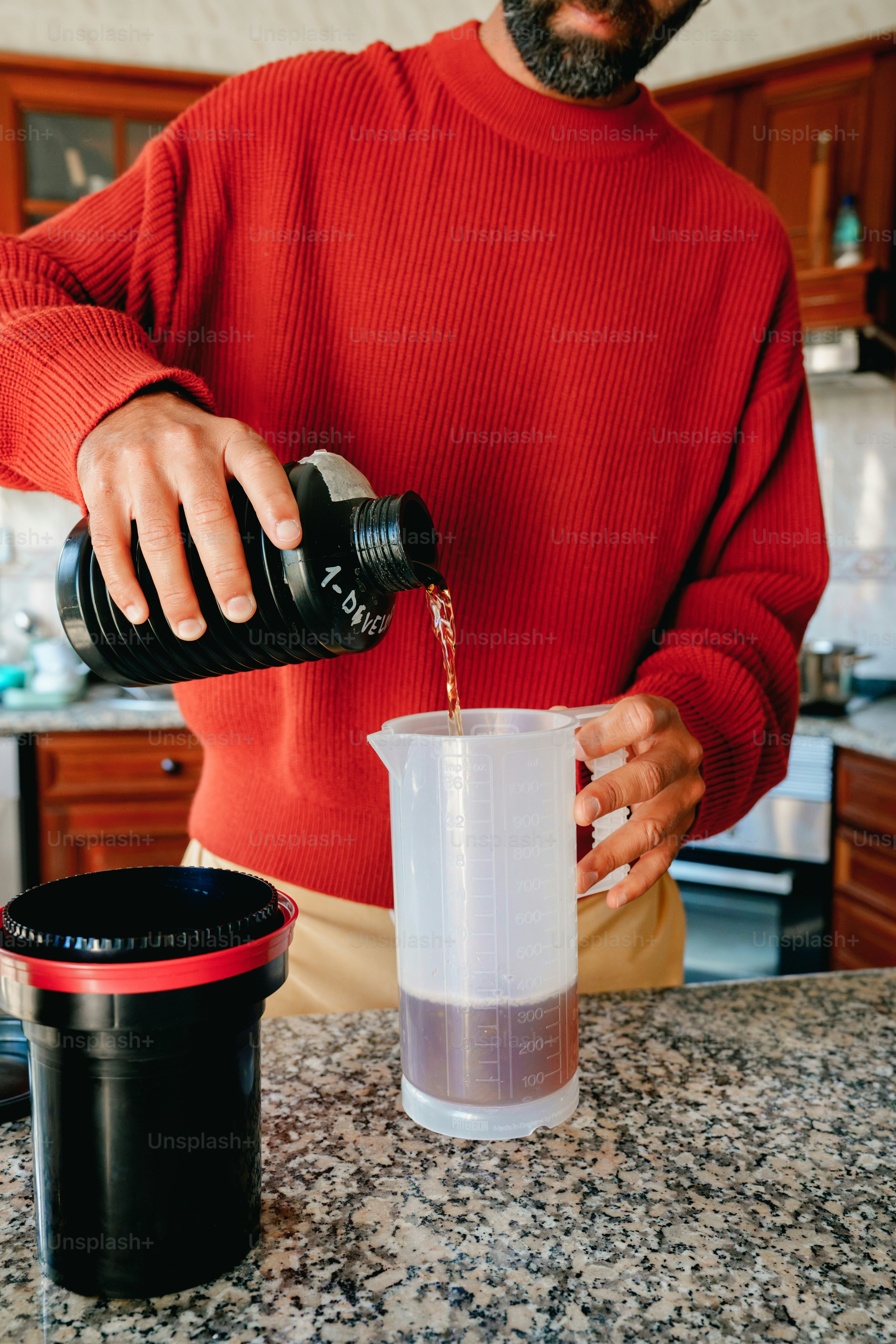 A person in a red sweater pouring dark liquid into a measuring cup
