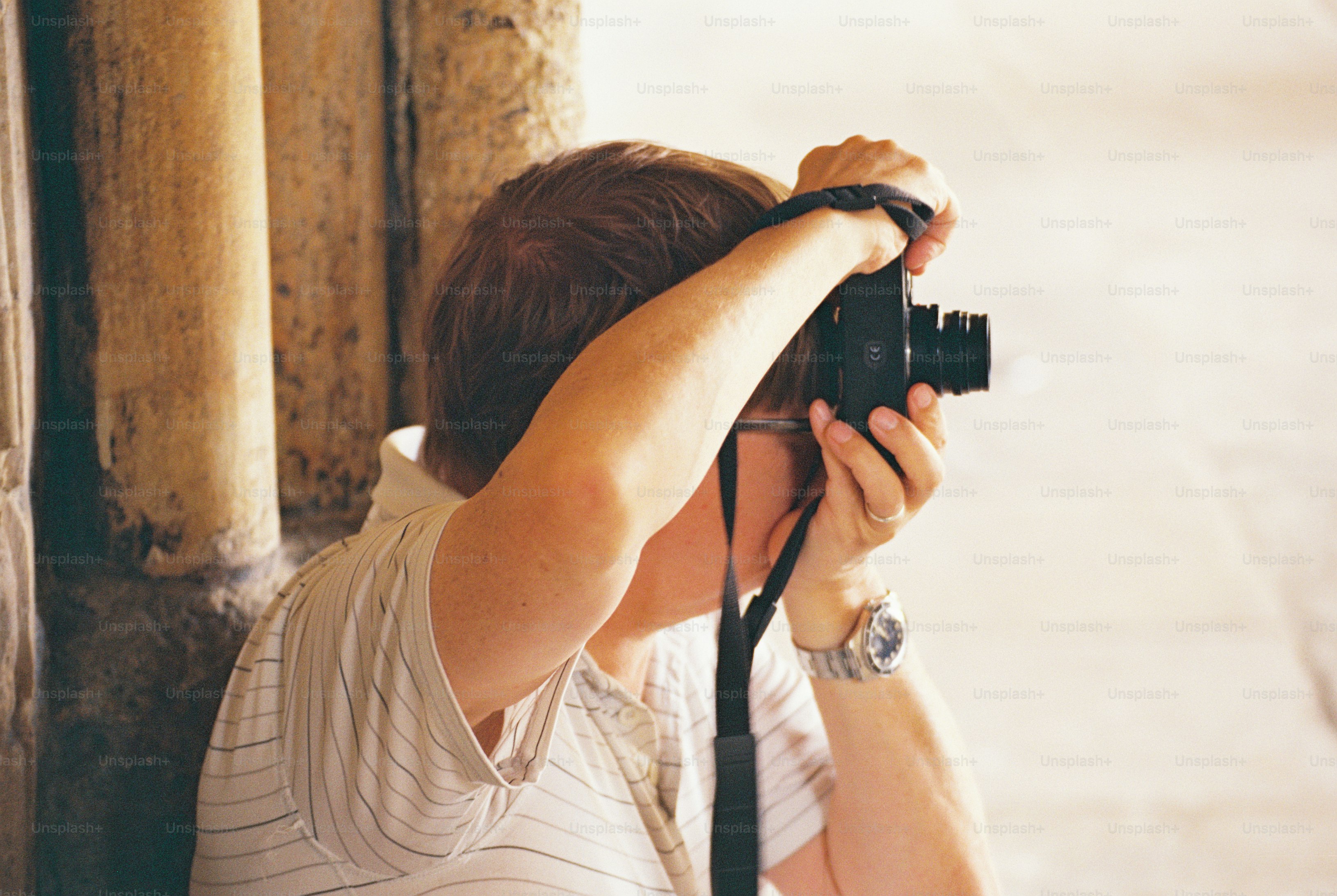 A person in a striped polo shirt holding a film camera to their eye