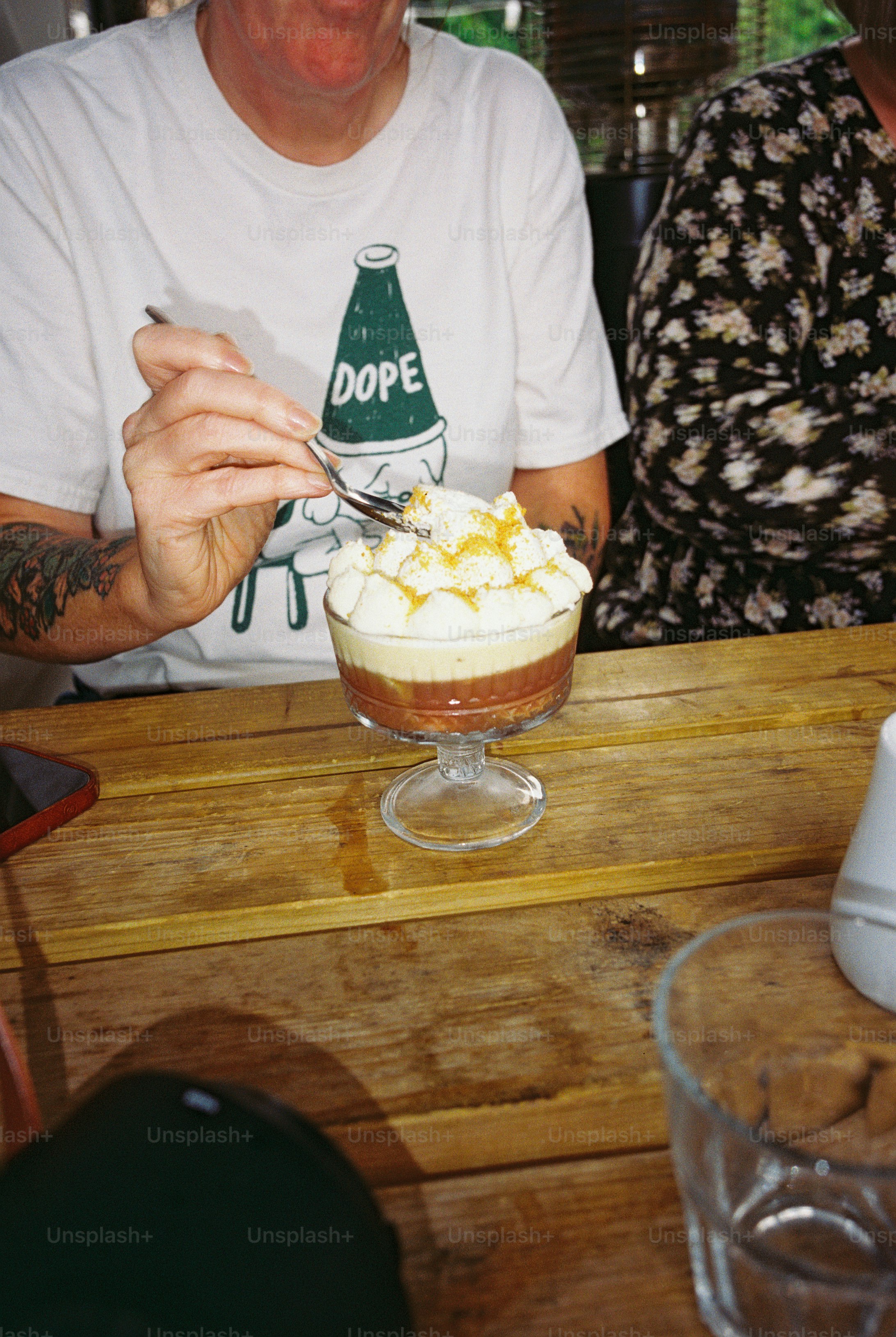 A person using a spoon to eat a layered dessert from a glass coupe