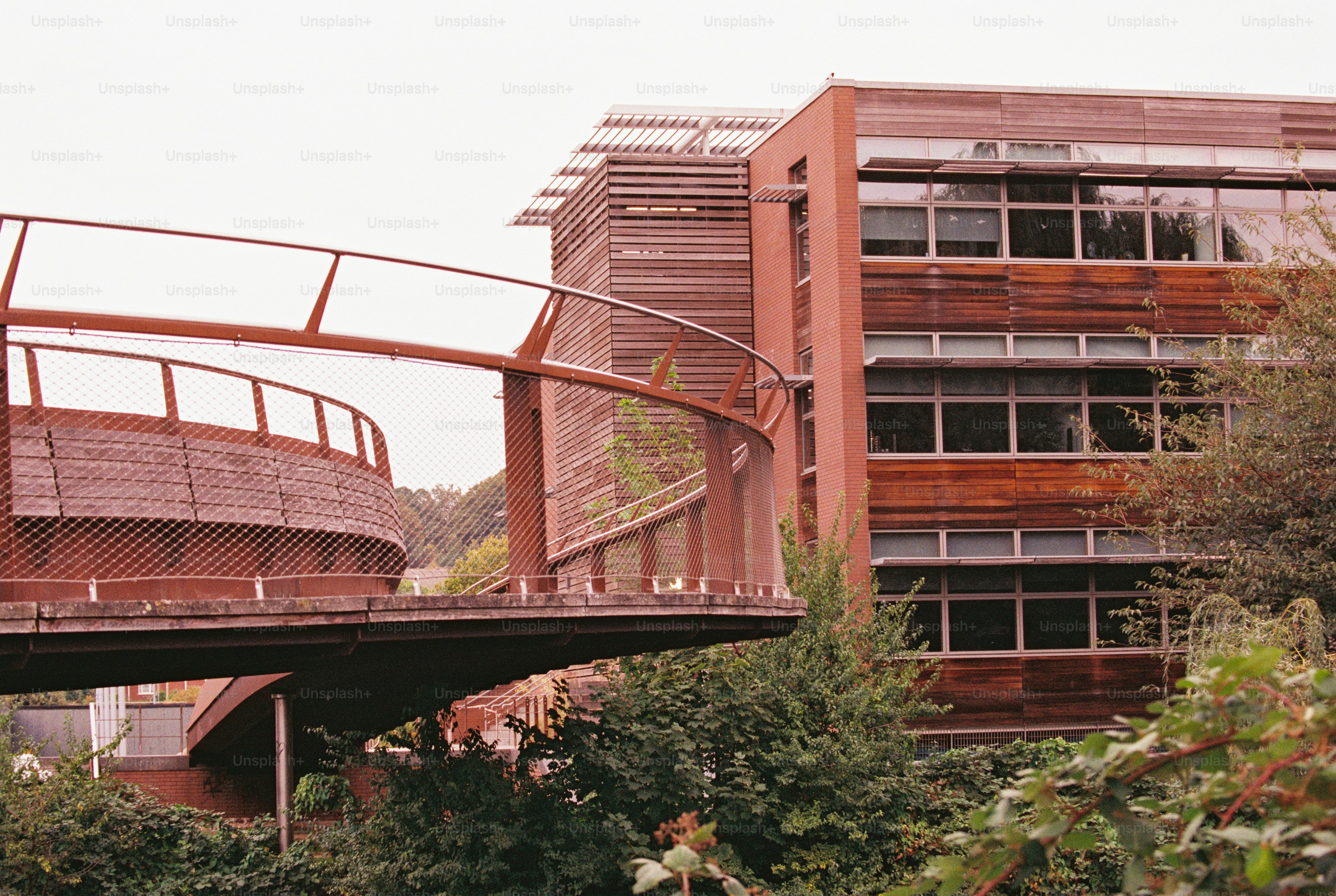 A rust-red curved footbridge ramp beside a modern brick and timber building in Norwich
