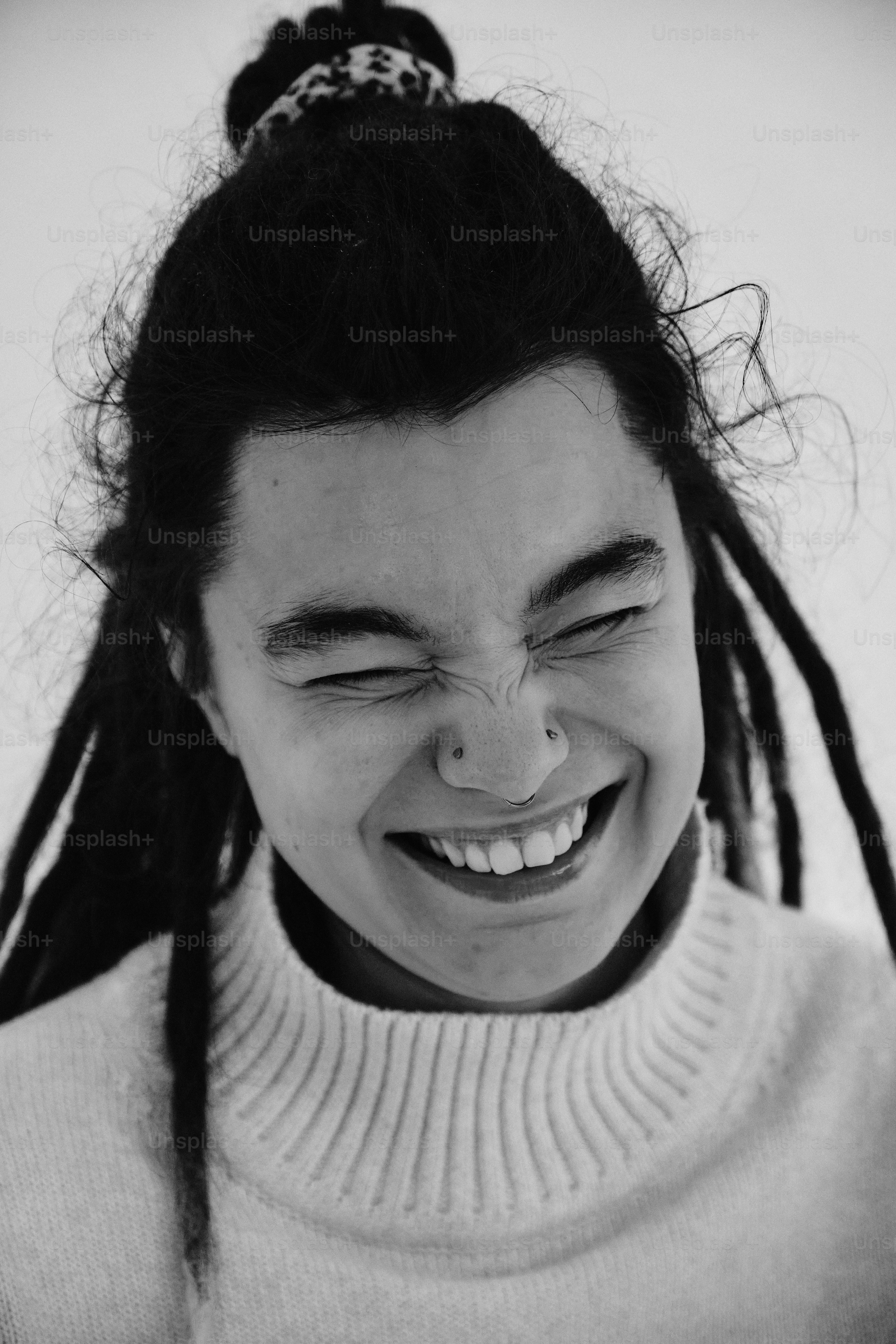 A person with dreadlocks and a nose ring laughing in a white sweater