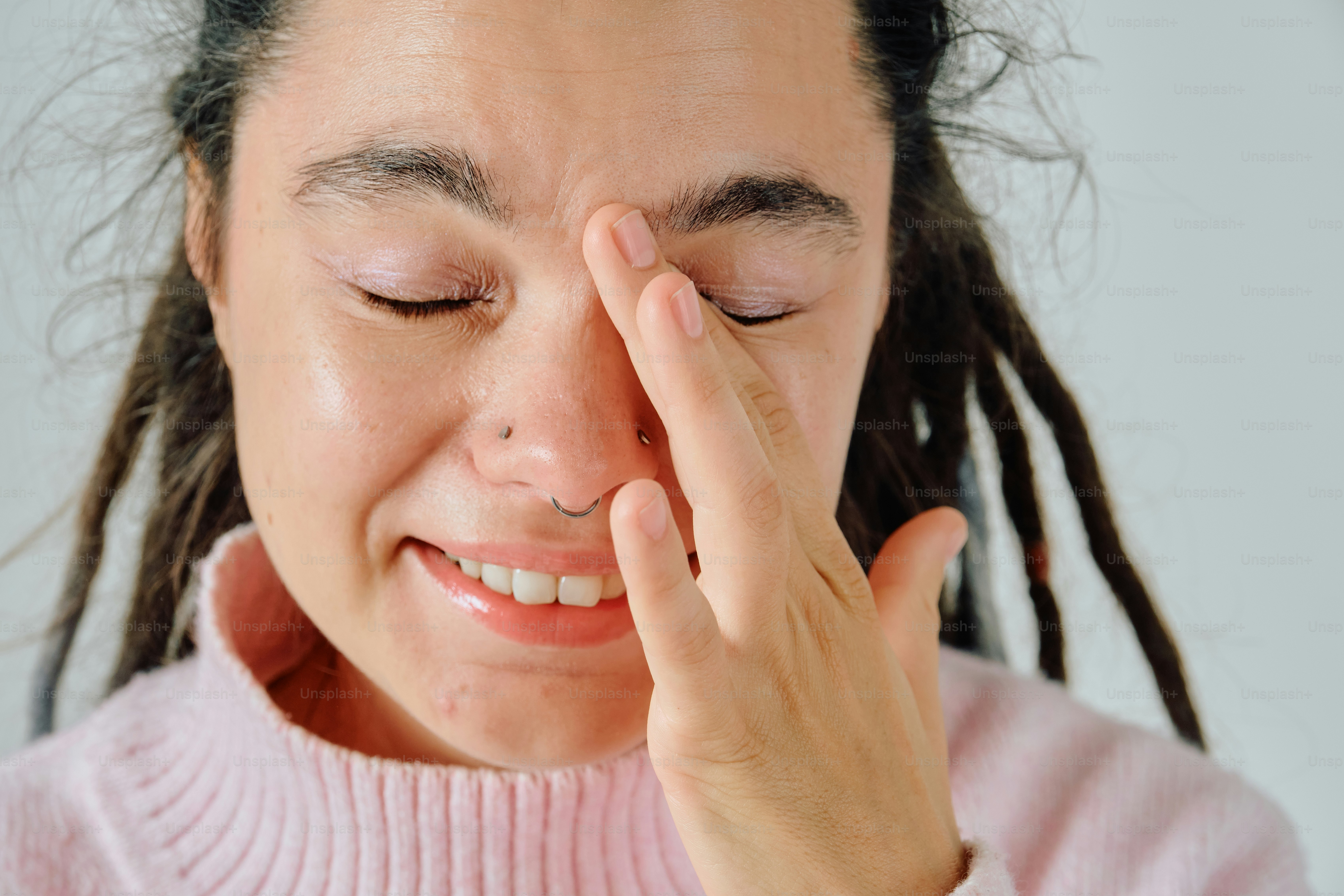 A person with dreadlocks and a nose ring touching their forehead with one hand