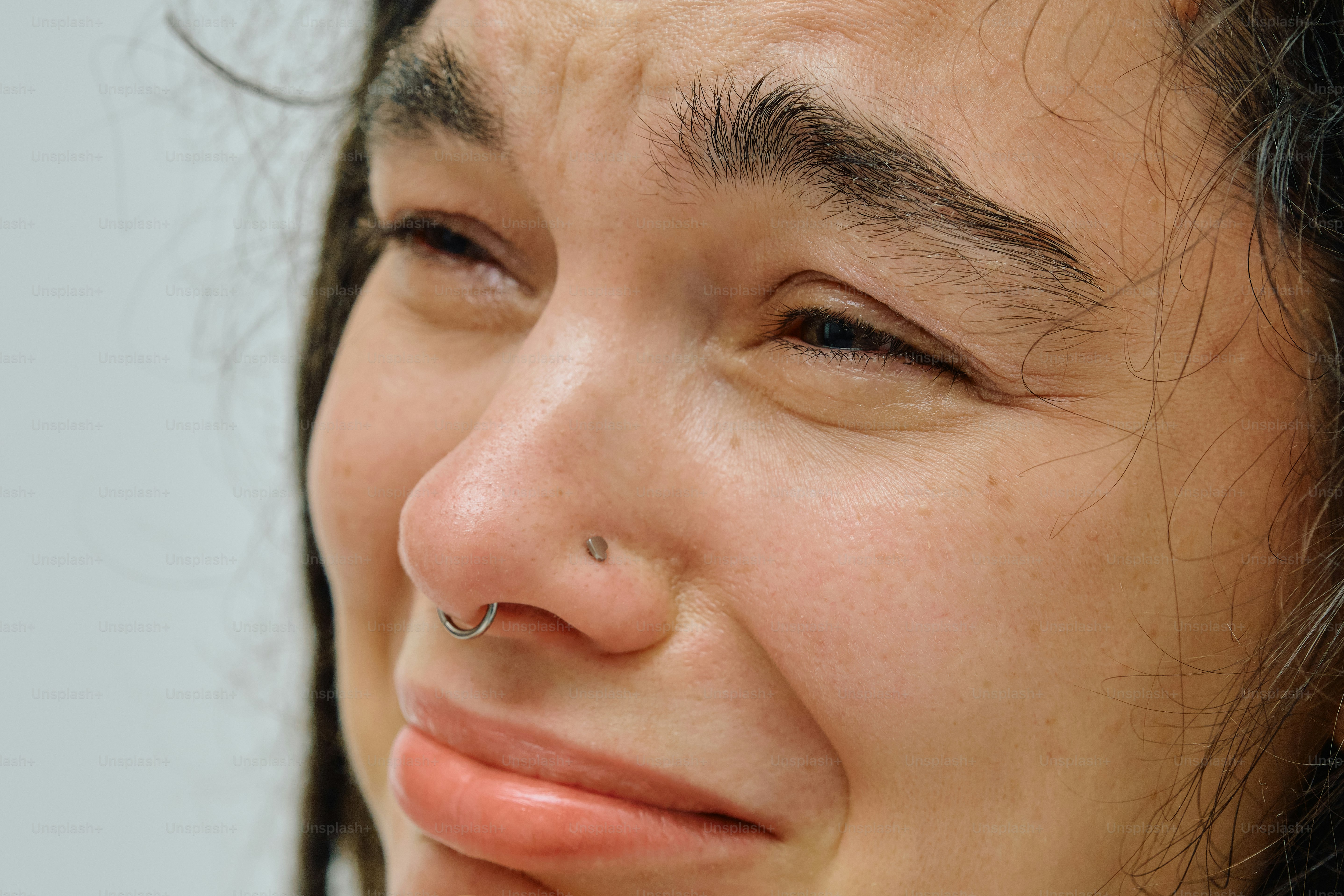 Close-up of a person with a nose ring crying with eyes squinted