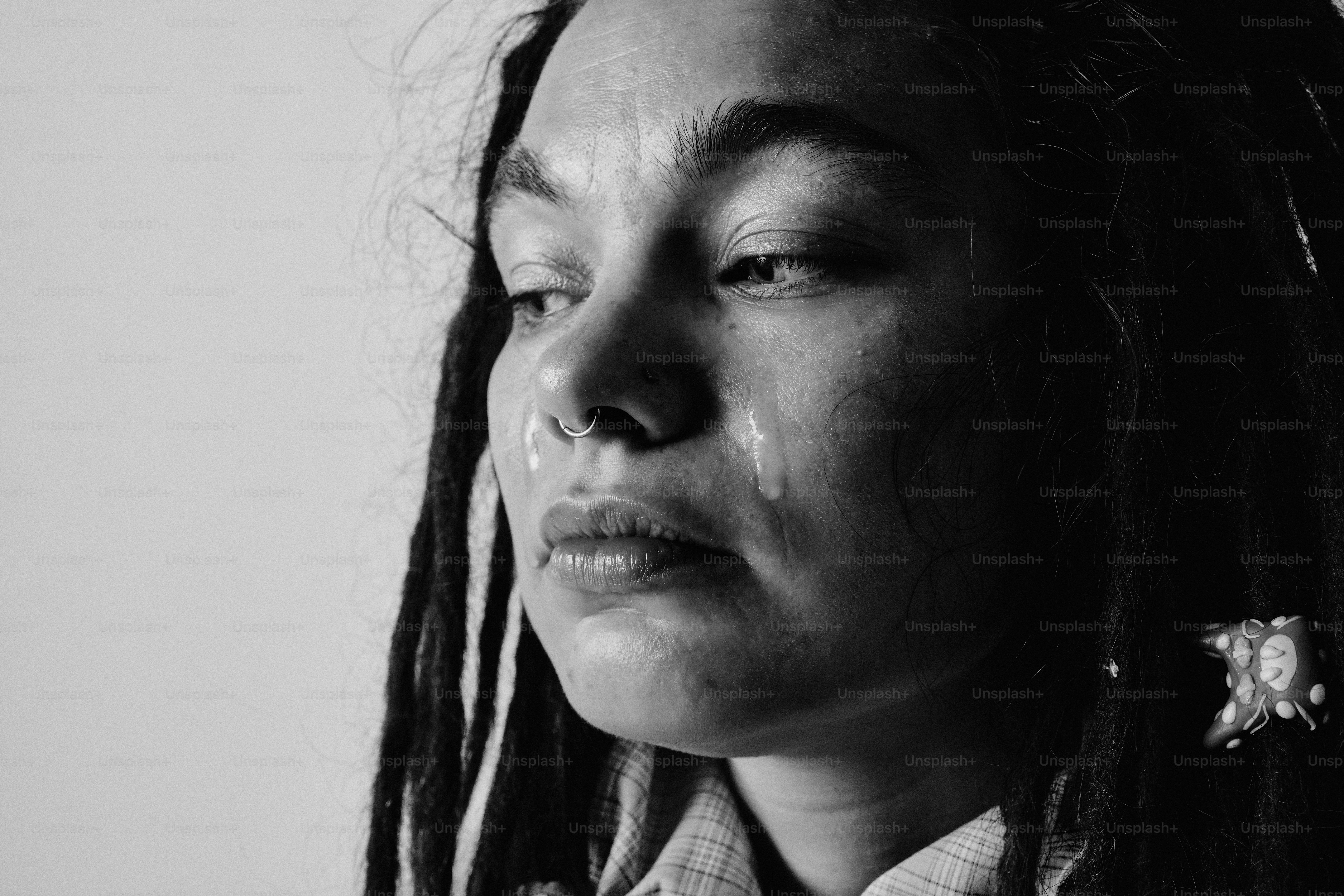A person with dreadlocks and a nose ring crying with a tear on their cheek