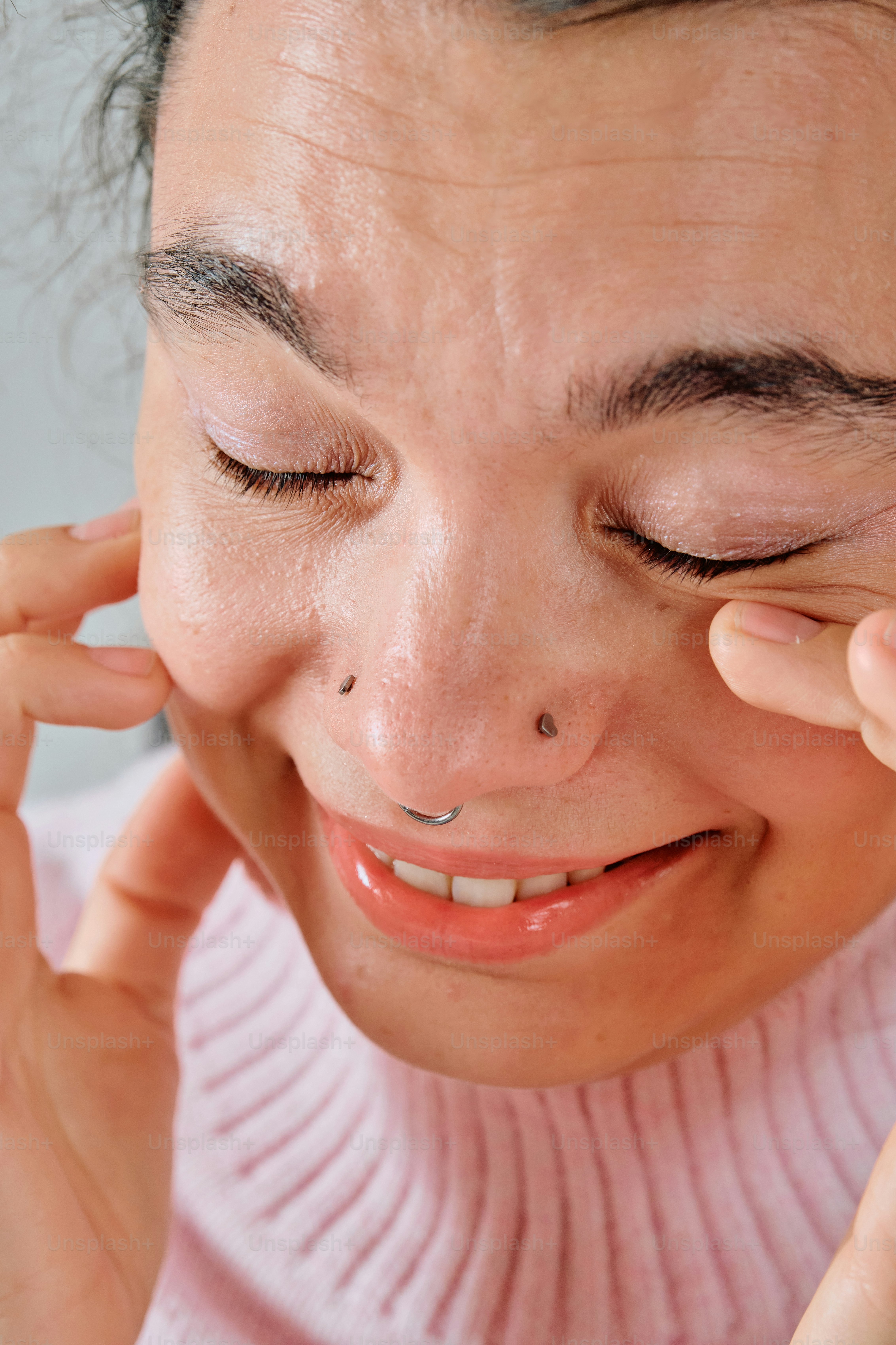A person with a nose piercing pulling their cheeks with their fingers
