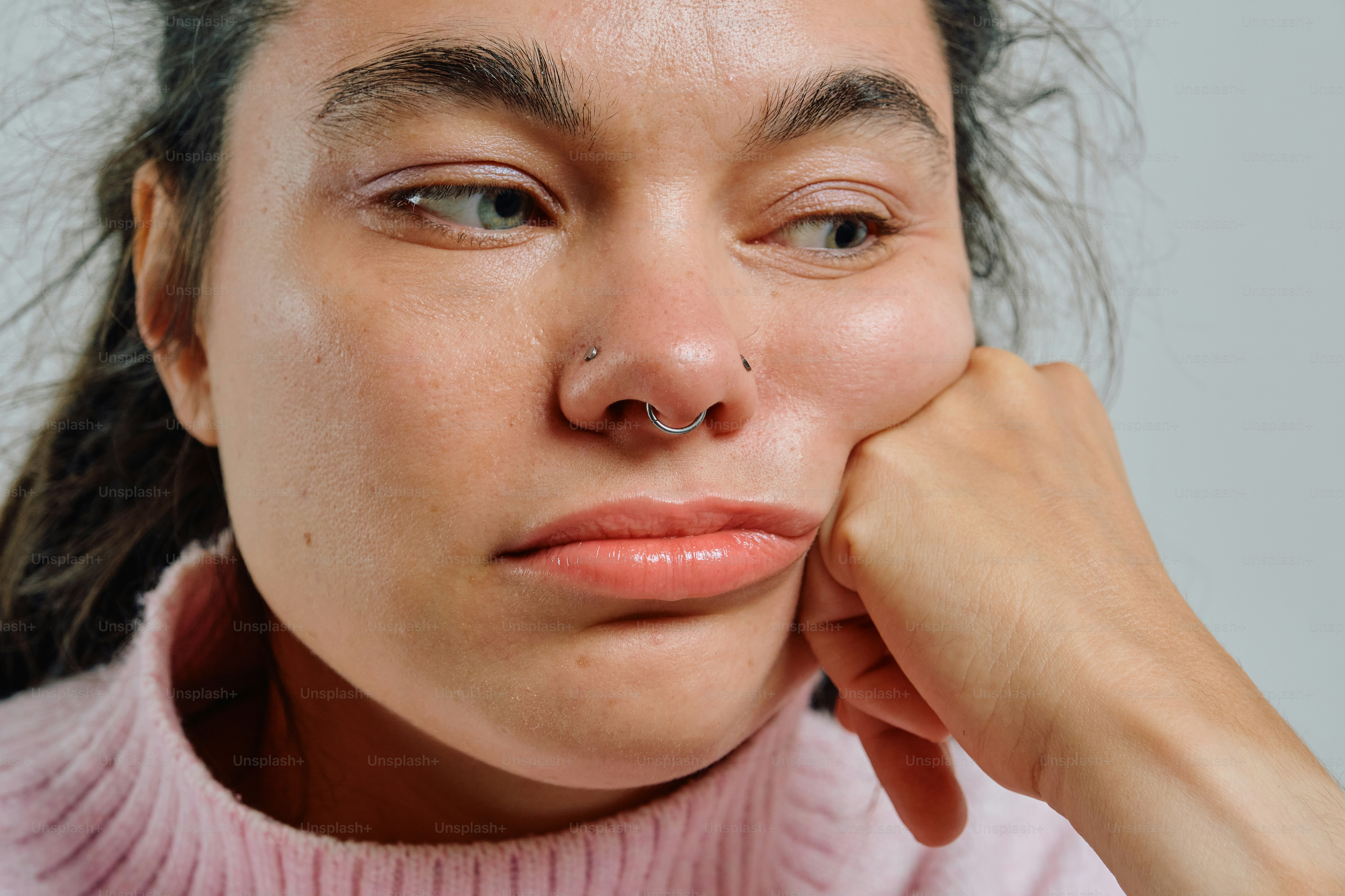 A person with a nose ring resting their chin on a hand