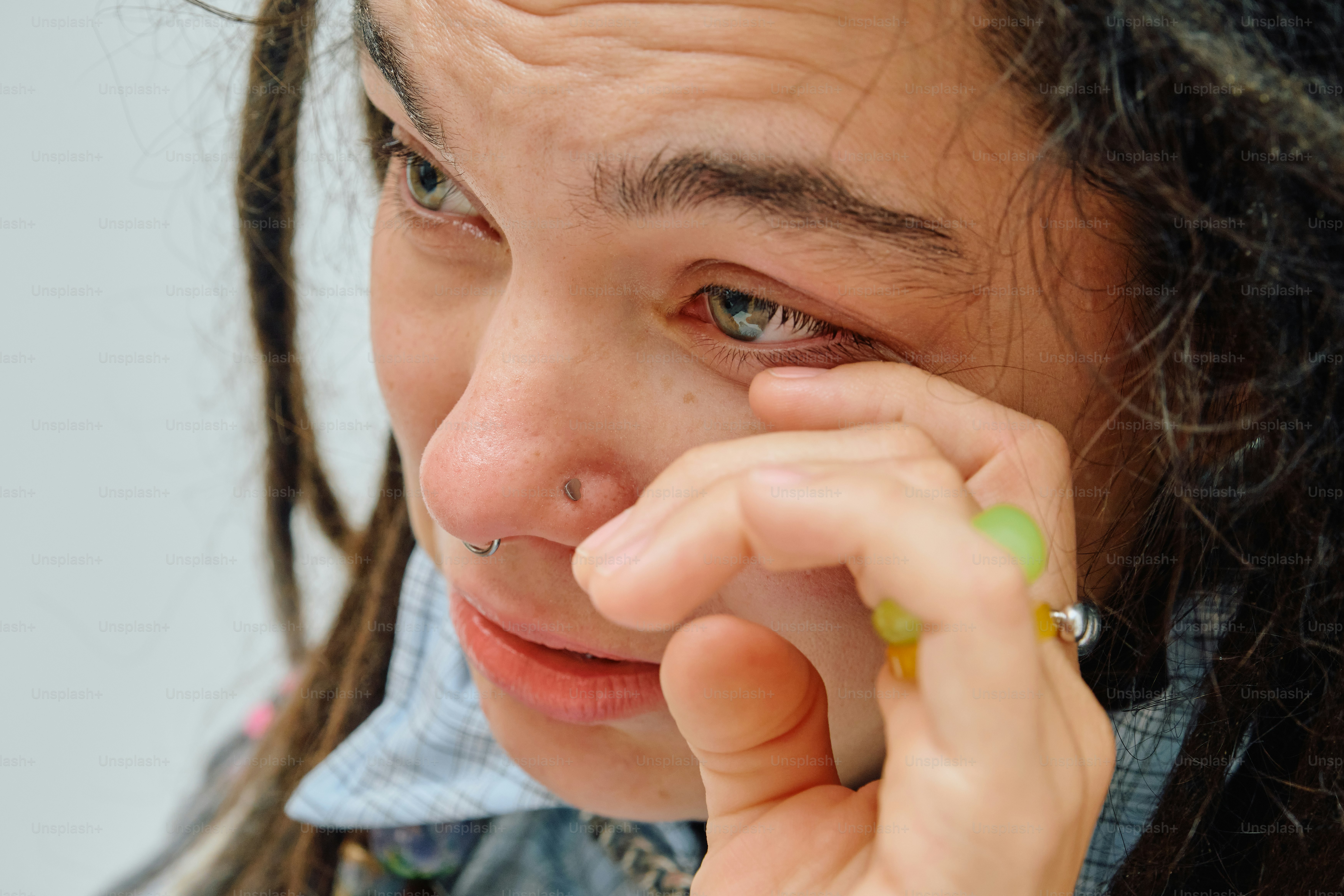 A person with dreadlocks wiping a tear from their eye with a ringed hand