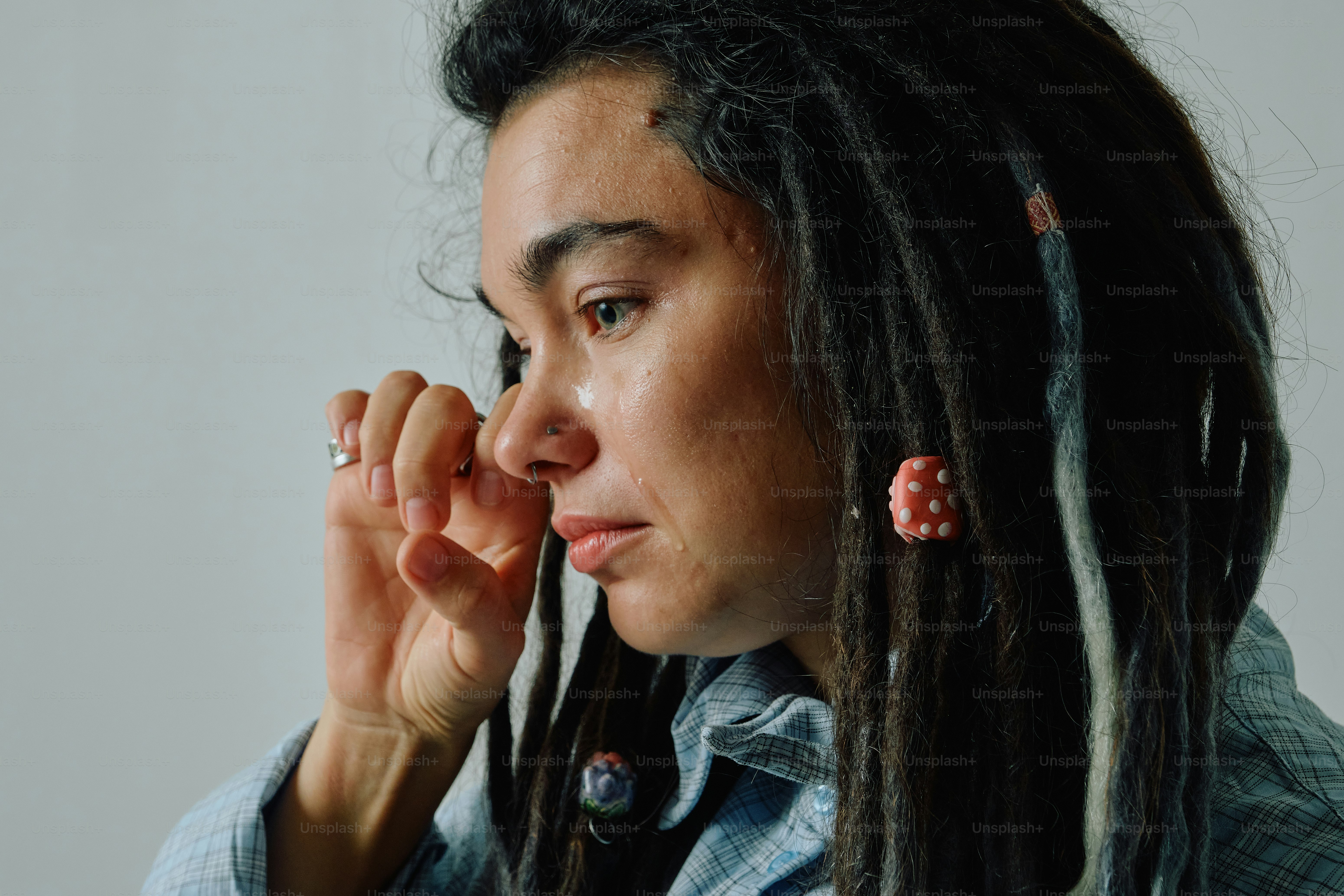 A person with dreadlocks wiping a tear from their cheek against a grey background