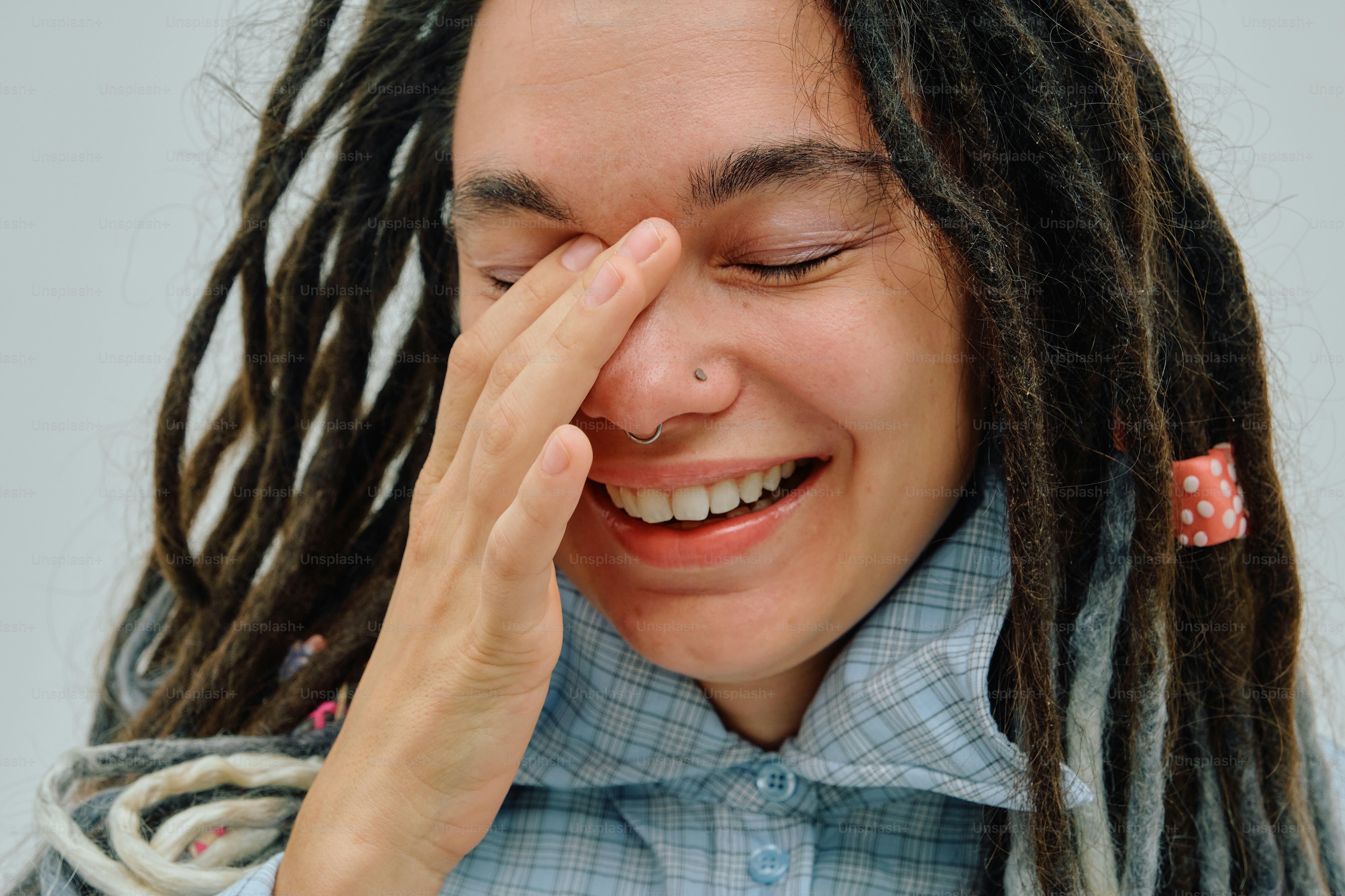 A person with dreadlocks laughing while covering one eye with their hand