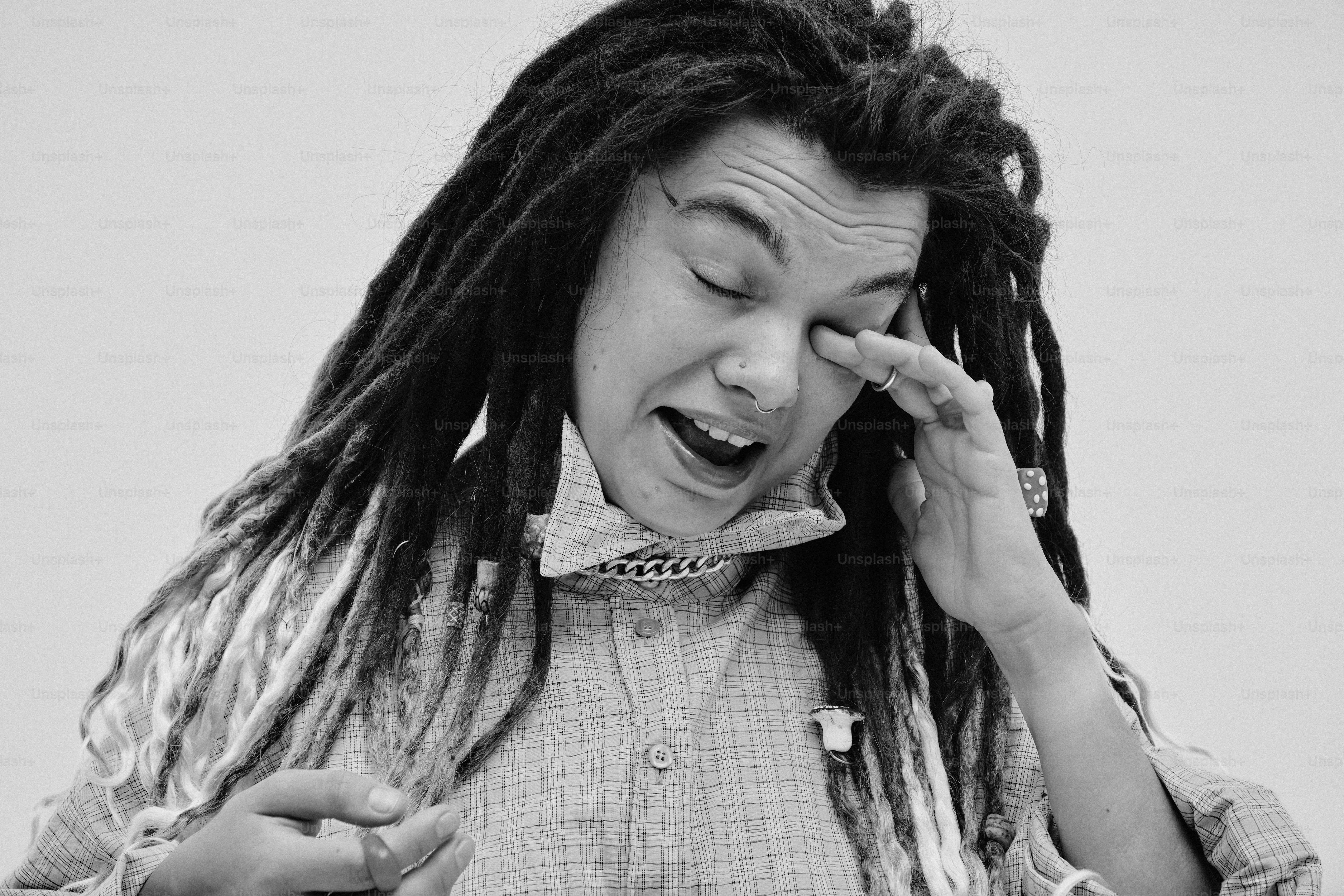 A person with dreadlocks rubbing their eye while wearing a plaid shirt
