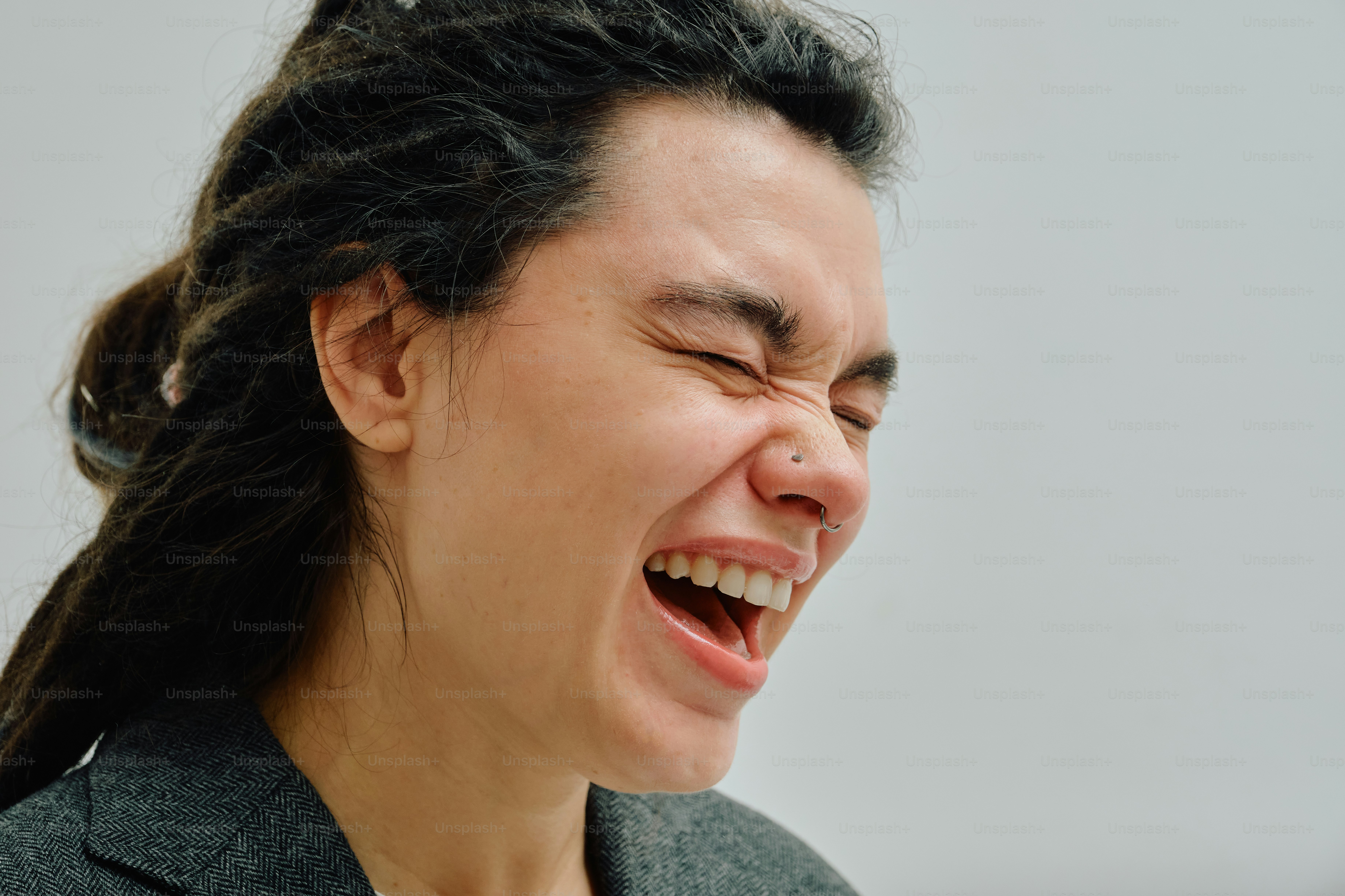 A person with dreadlocks and a nose ring laughing with eyes closed