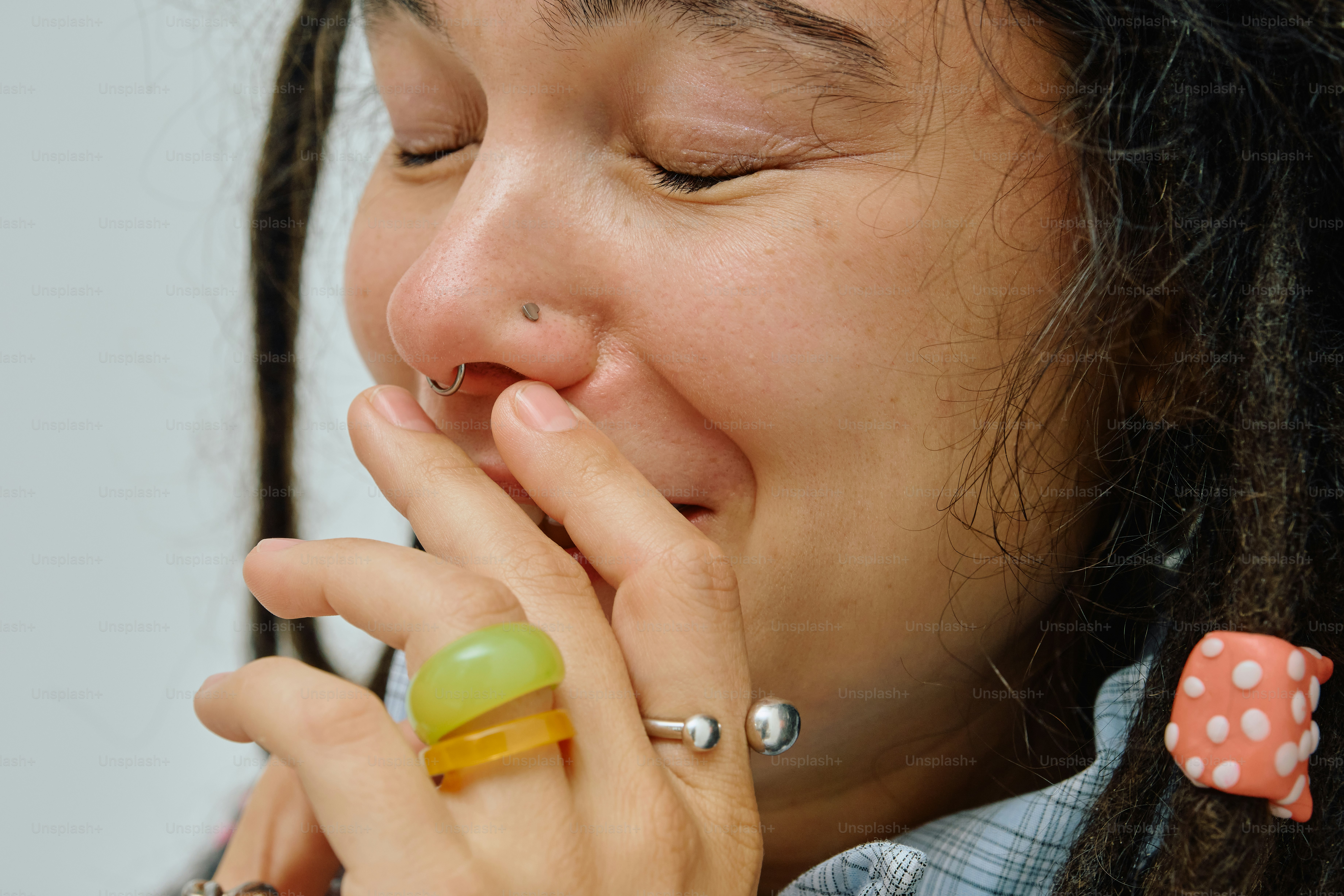 A person with dreadlocks and a nose ring laughing with a hand covering their mouth