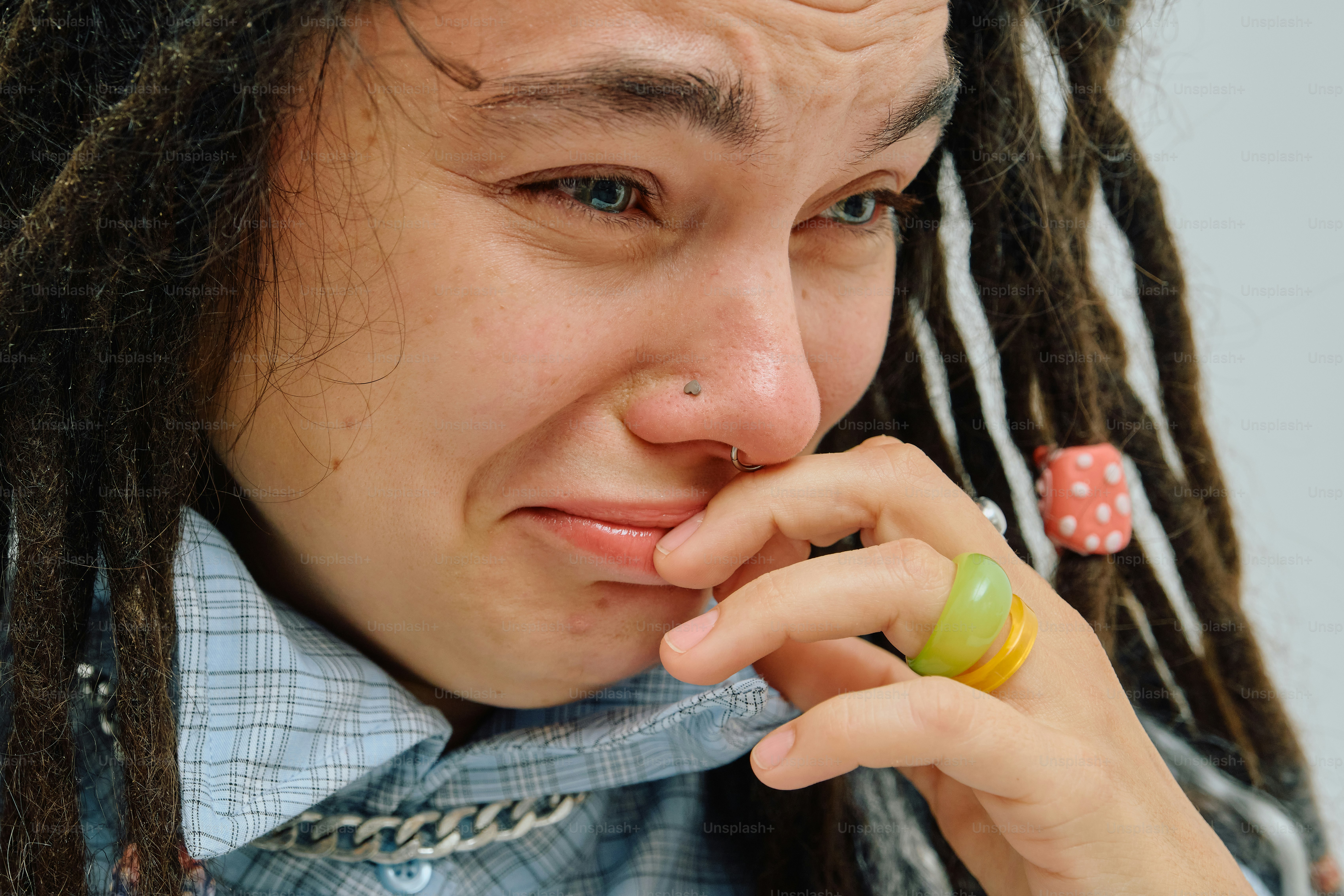A person with dreadlocks and a nose ring crying with a hand near their mouth