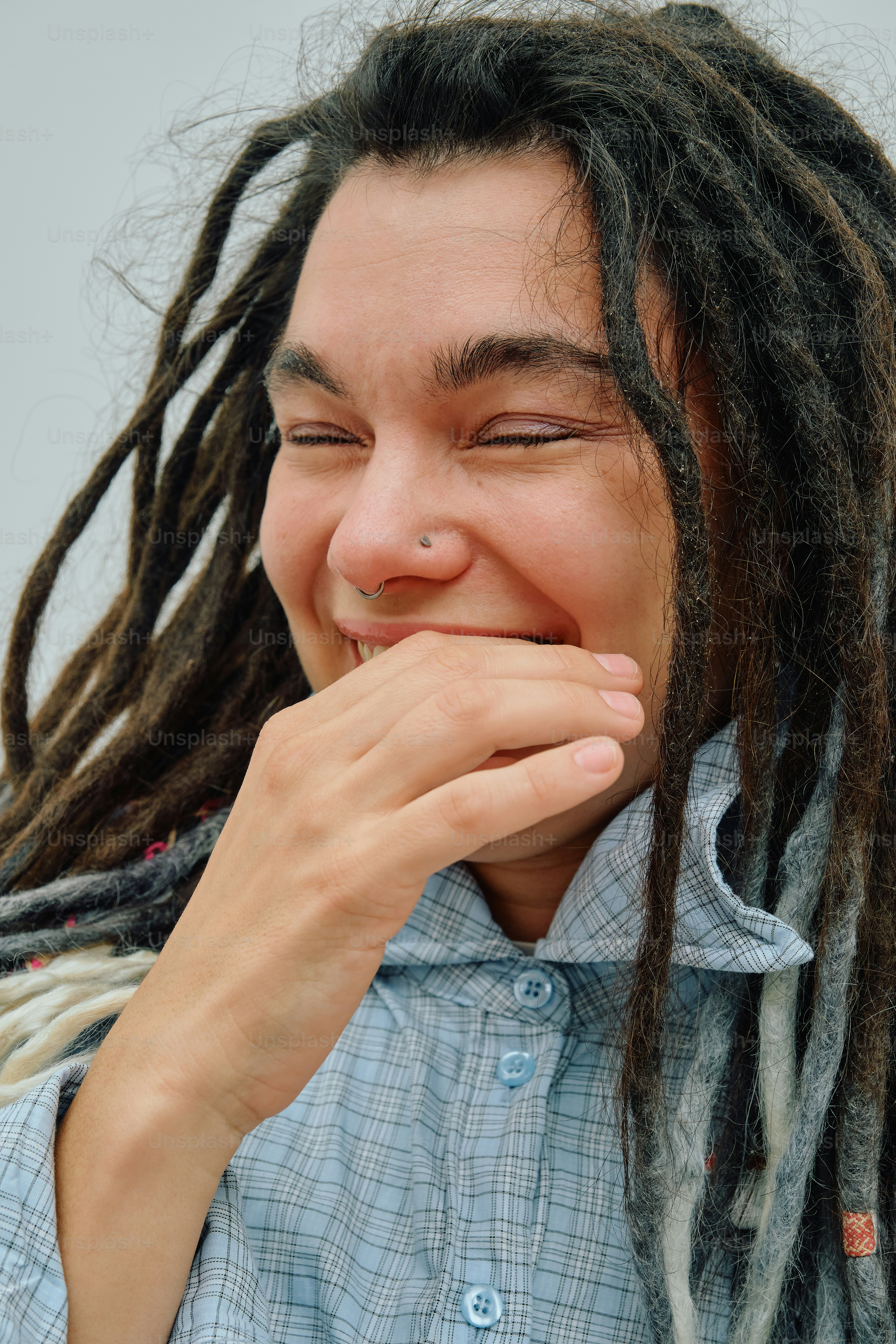 A person with dreadlocks laughing with a hand covering their mouth