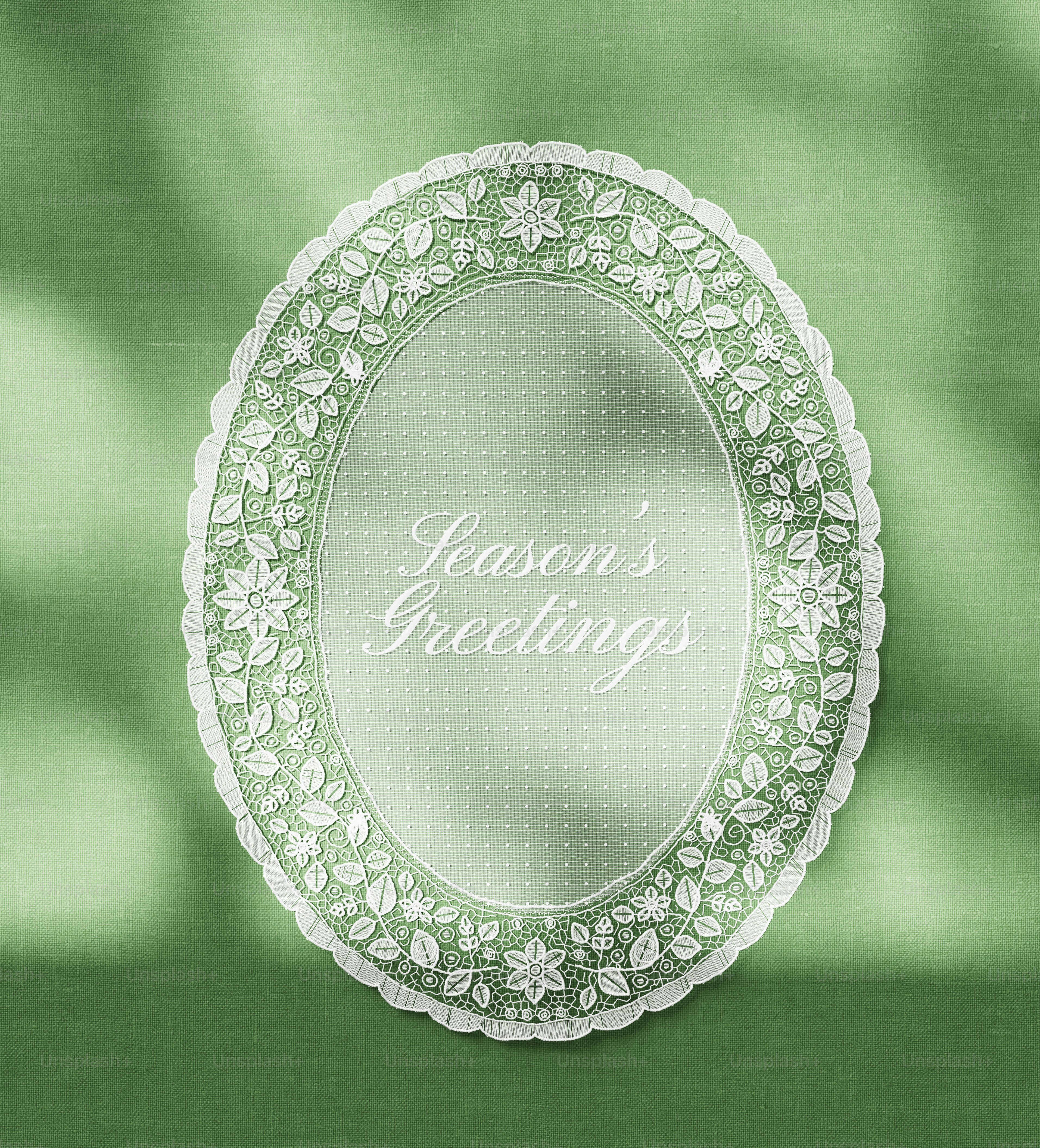 An oval white lace frame with floral patterns on a green fabric background