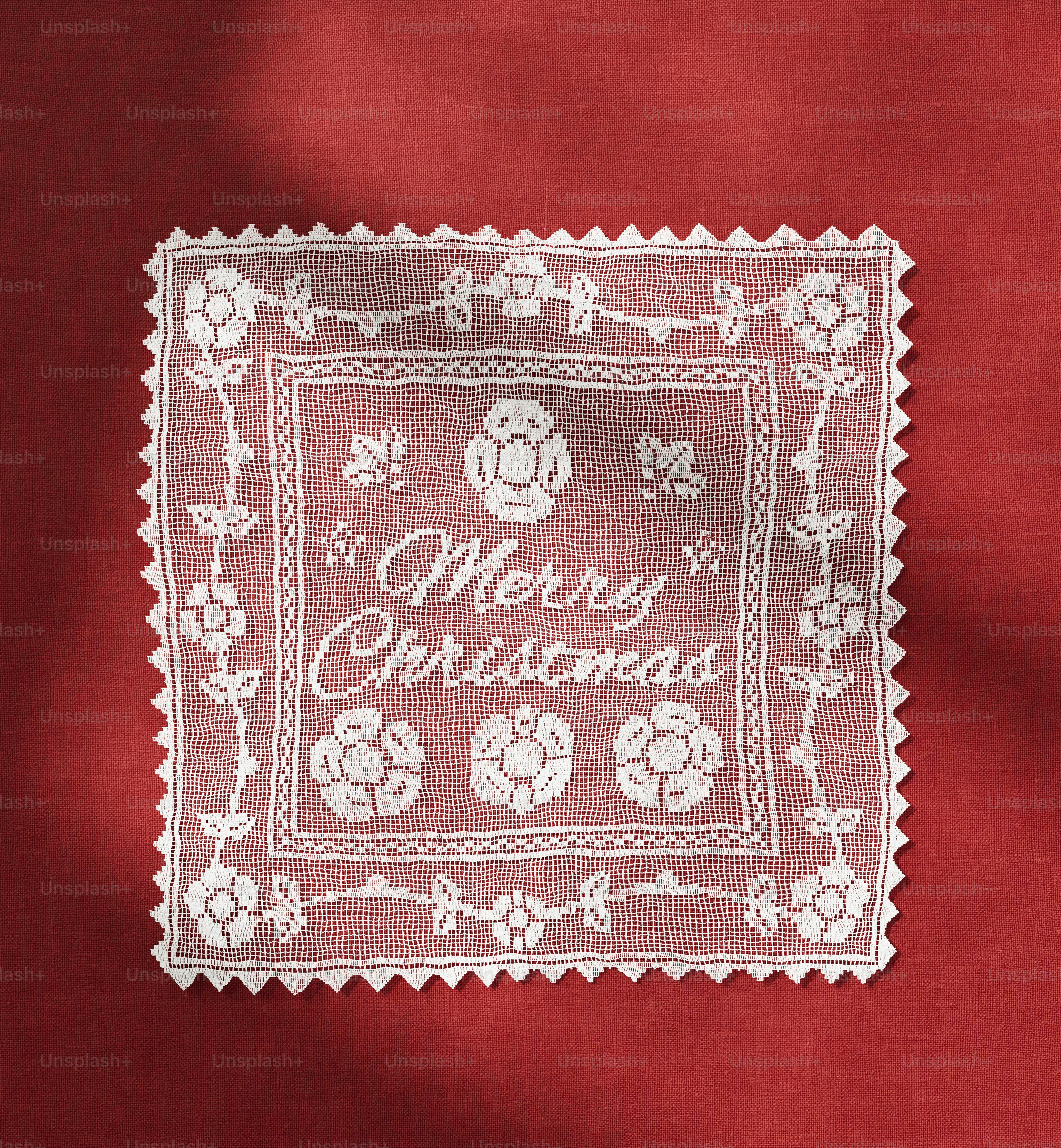 A white lace doily with Merry Christmas text on a red fabric background