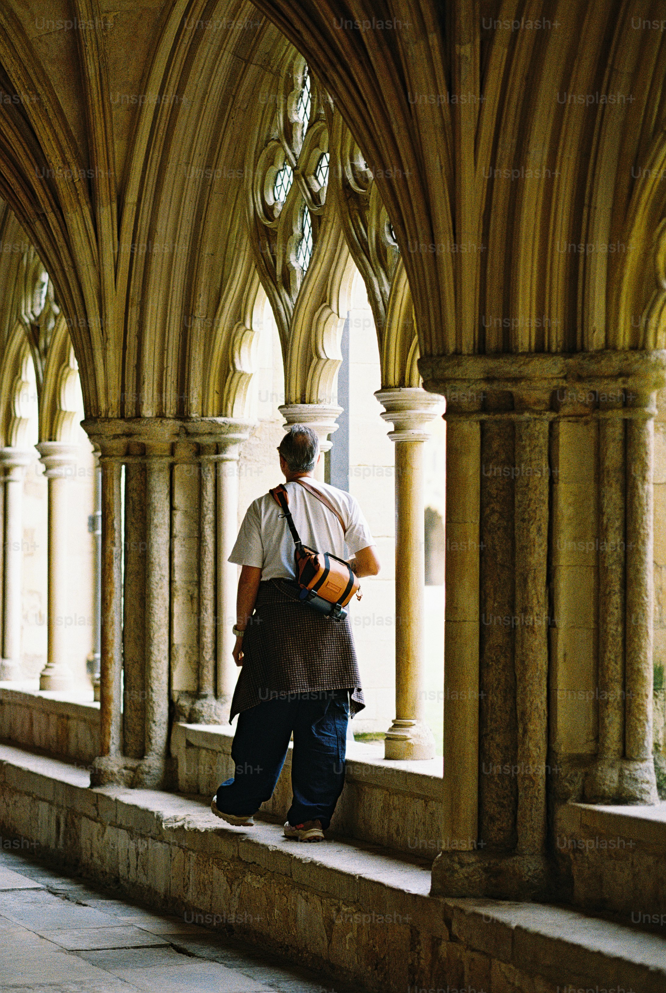 A person with a camera bag standing in a stone cloister with arched columns
