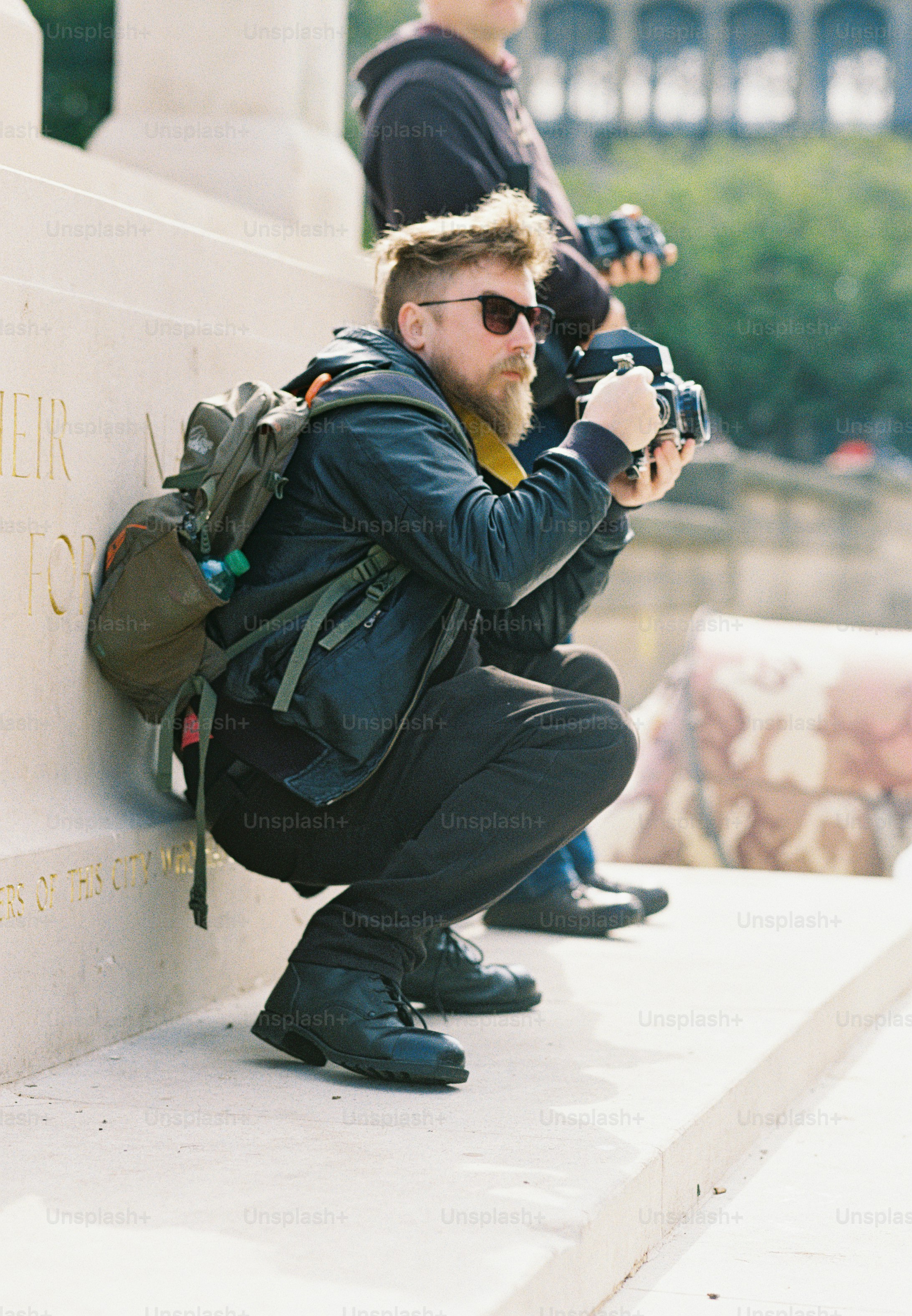 A bearded man with sunglasses crouching to take a photograph with a medium format camera