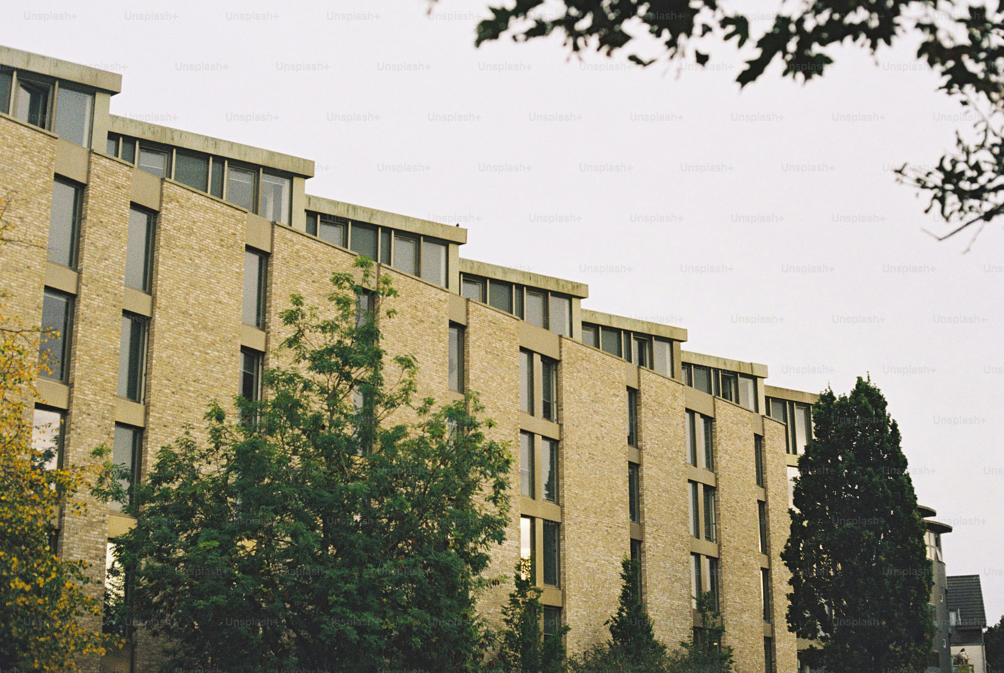 A modern brick apartment building with tiered rooflines and green trees in front