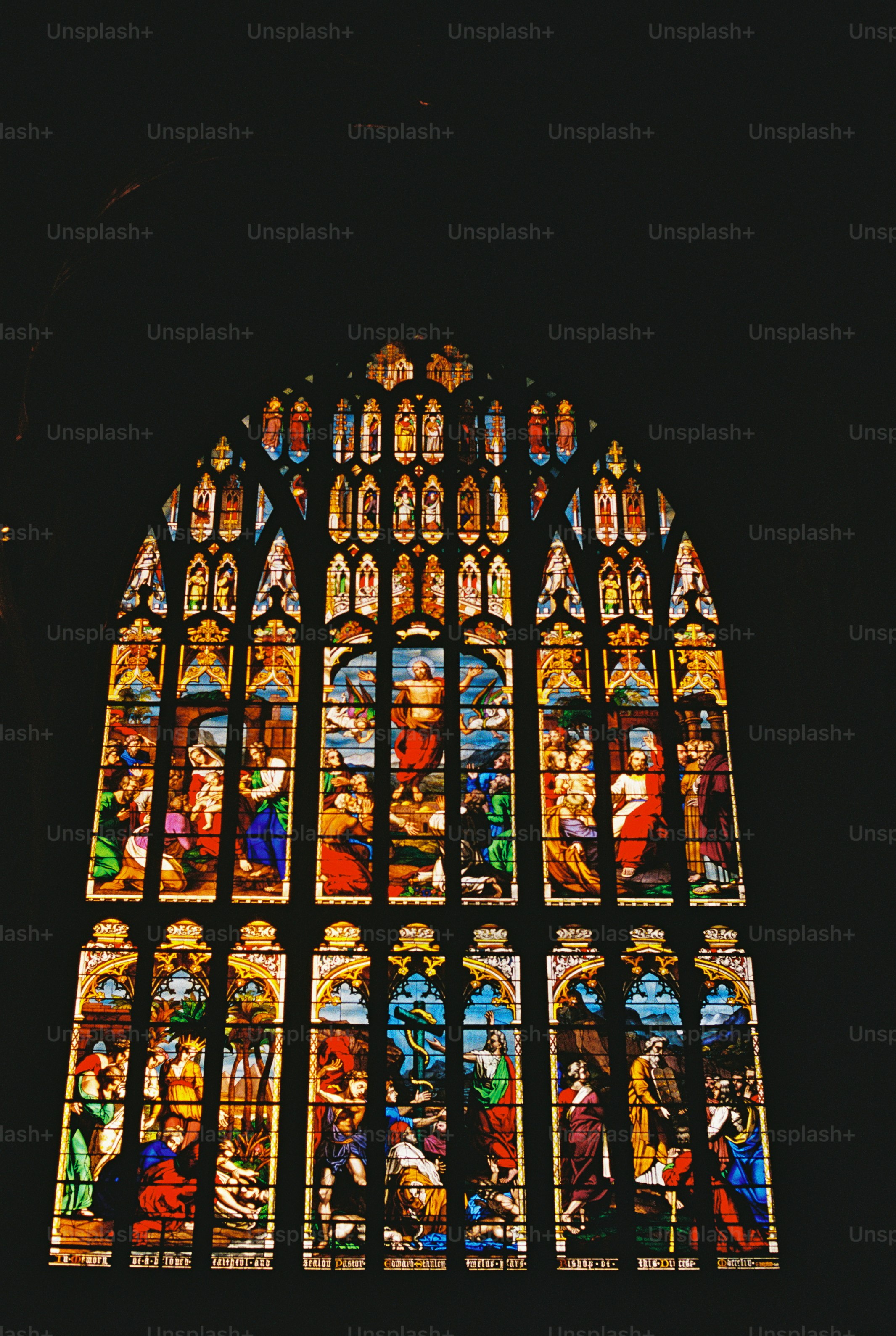 A large arched stained glass window depicting religious scenes in vibrant colors
