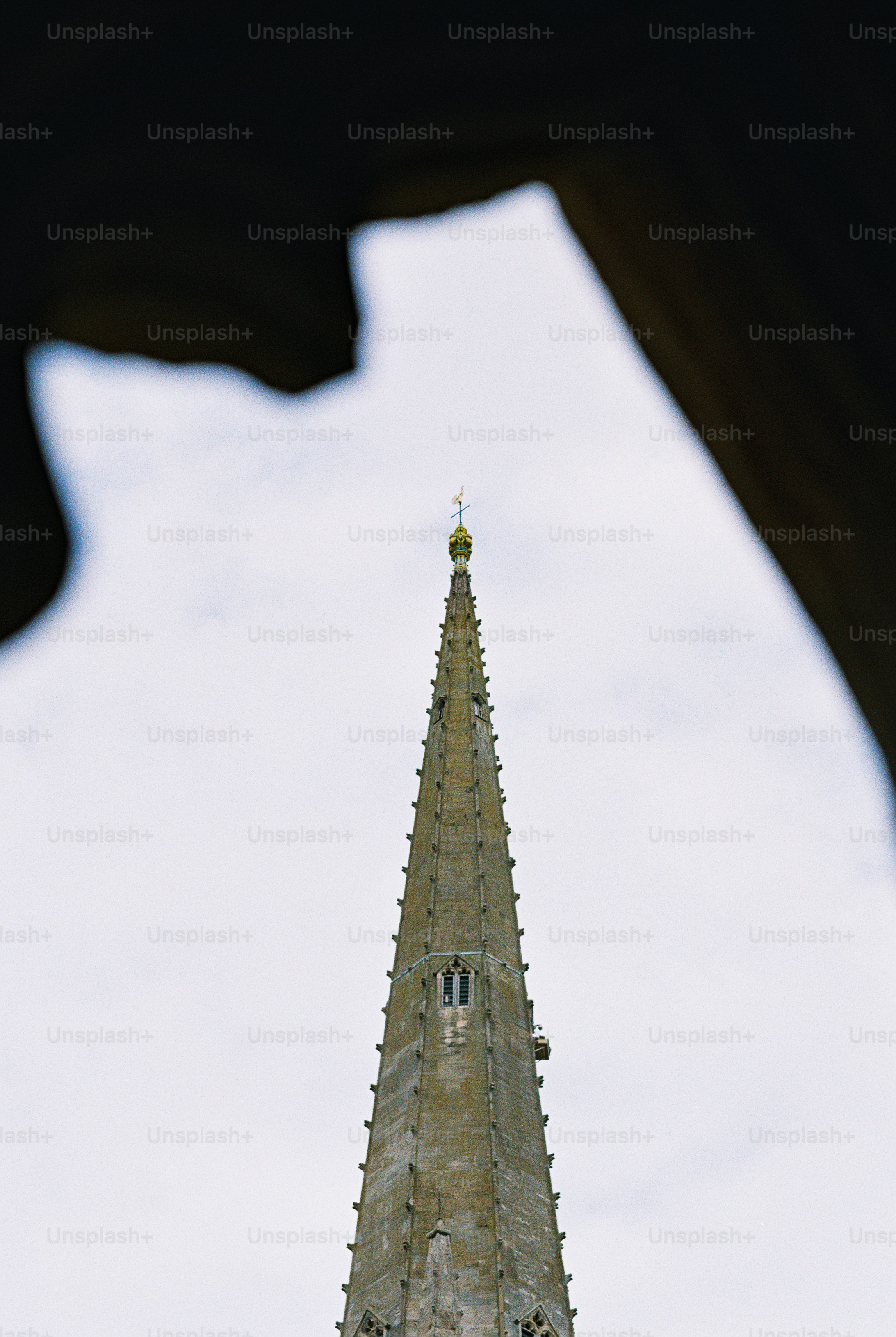 A stone church spire with a golden finial against a pale sky