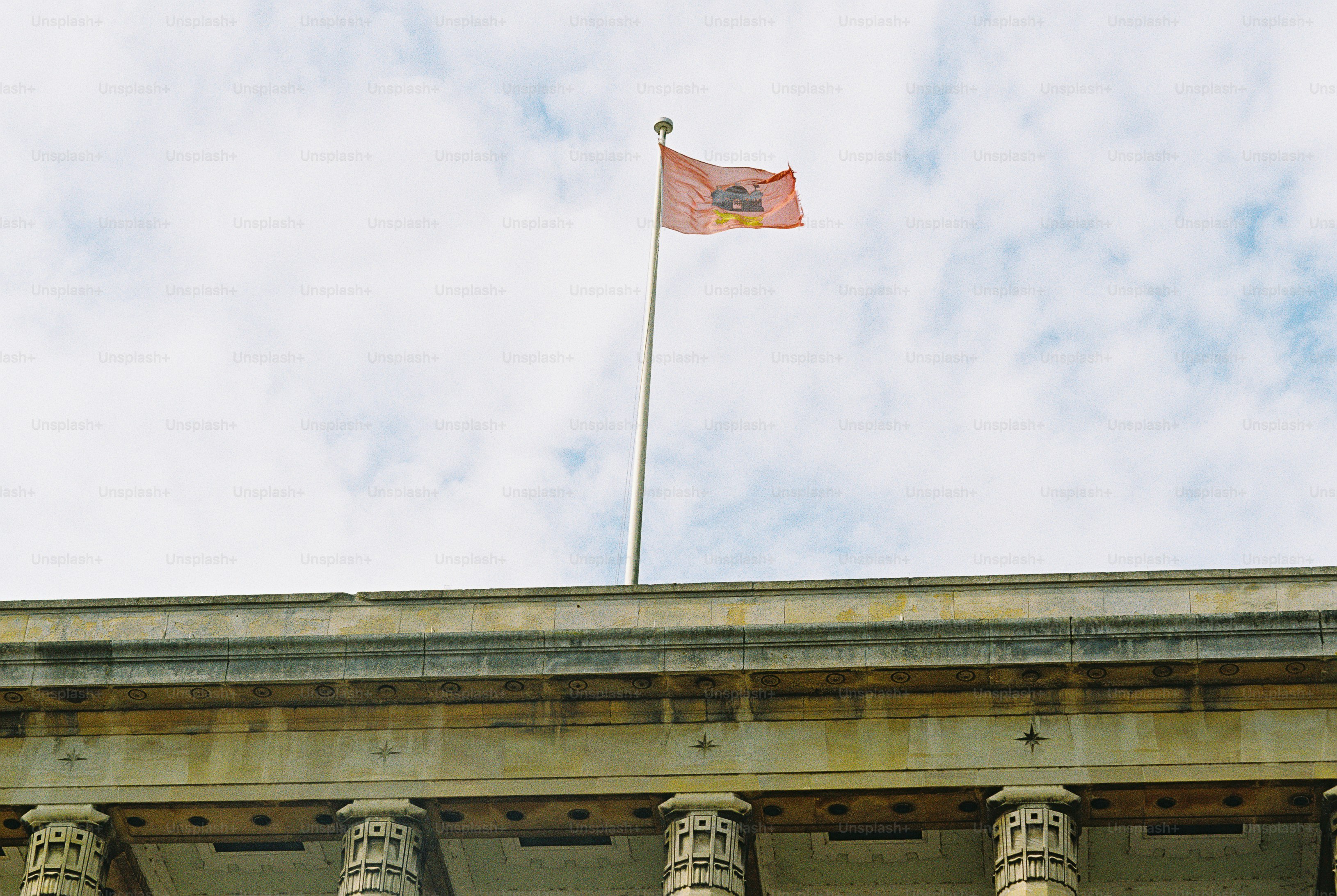 A pale orange flag flying on a tall pole above a stone building