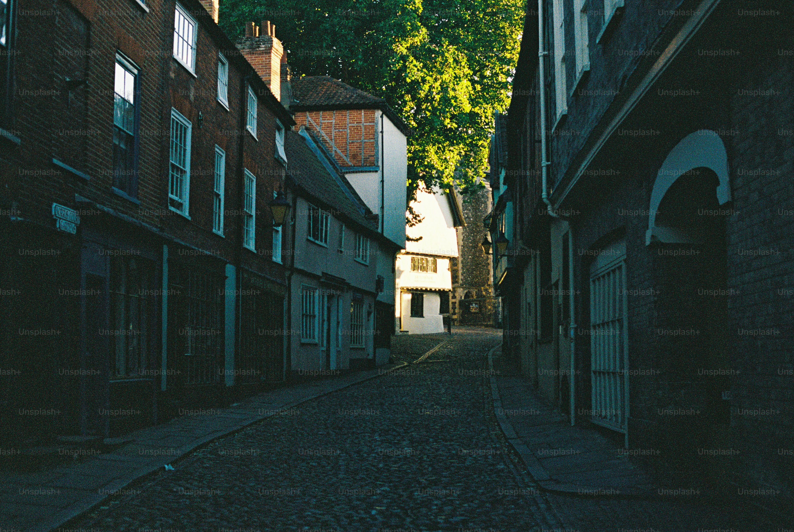 A narrow cobblestone street lined with historic brick and timber-framed buildings in low light