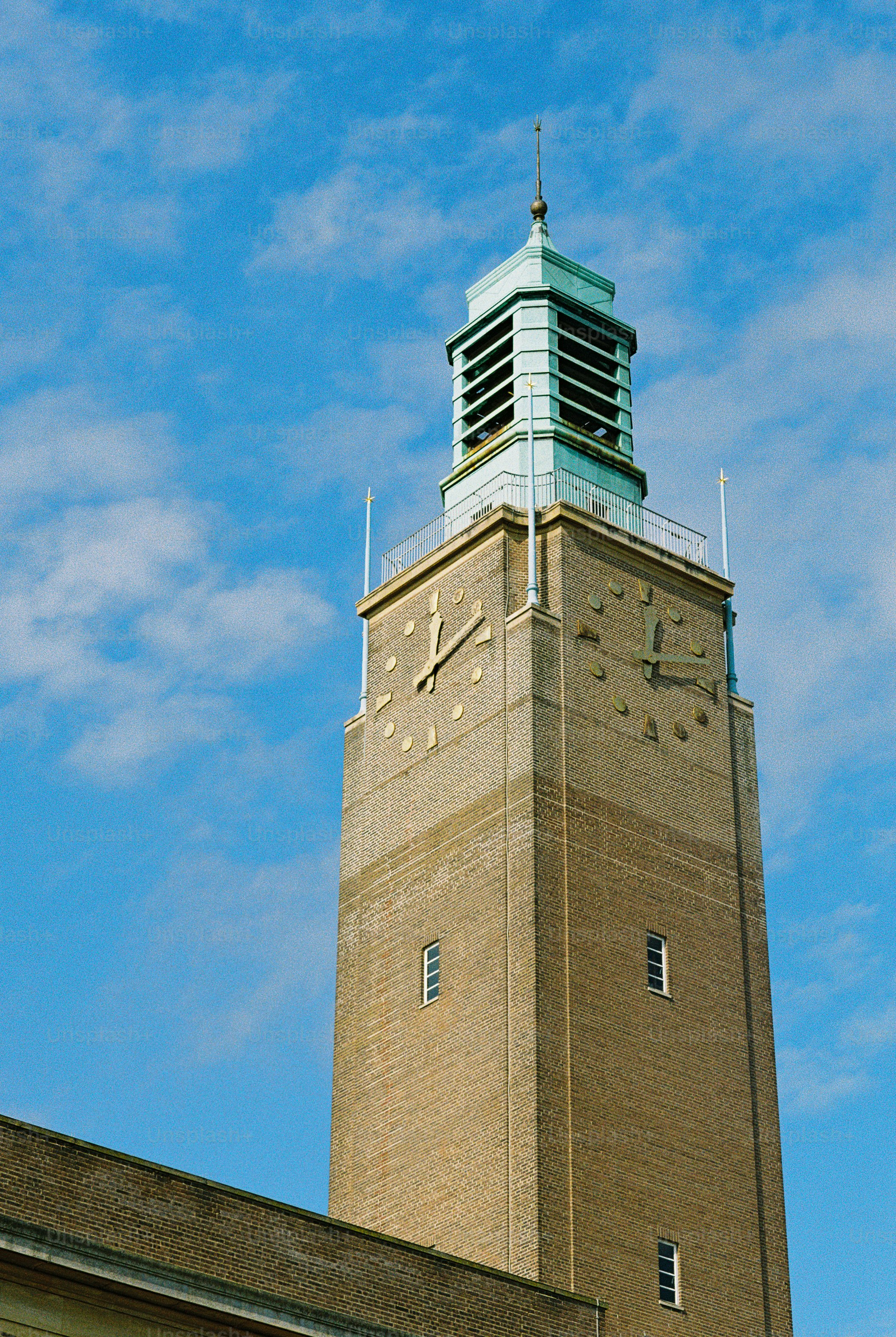 A tall brick clock tower with a green metal belfry against a blue sky