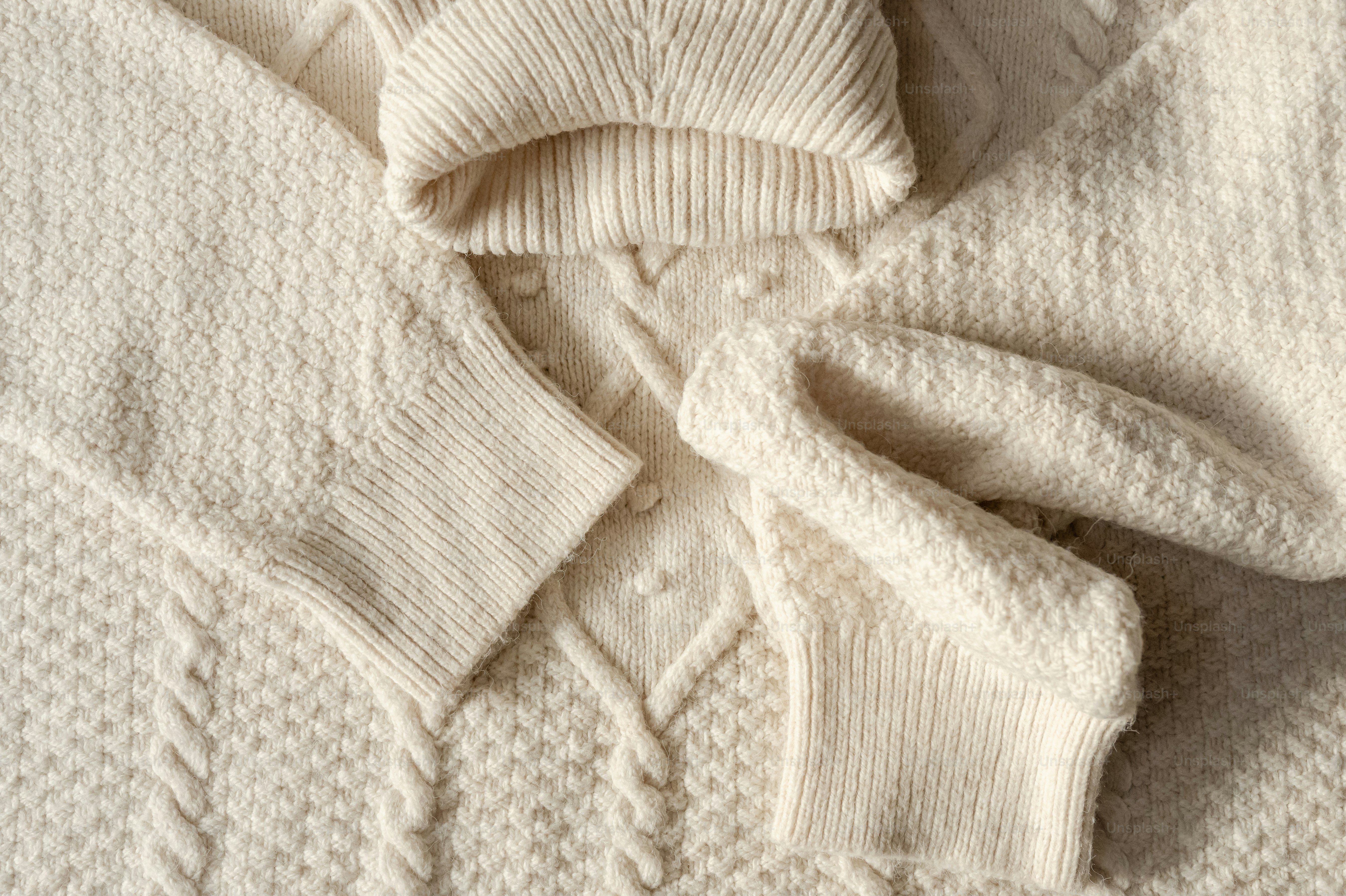 A close-up of a cream-colored cable knit sweater with a textured pattern