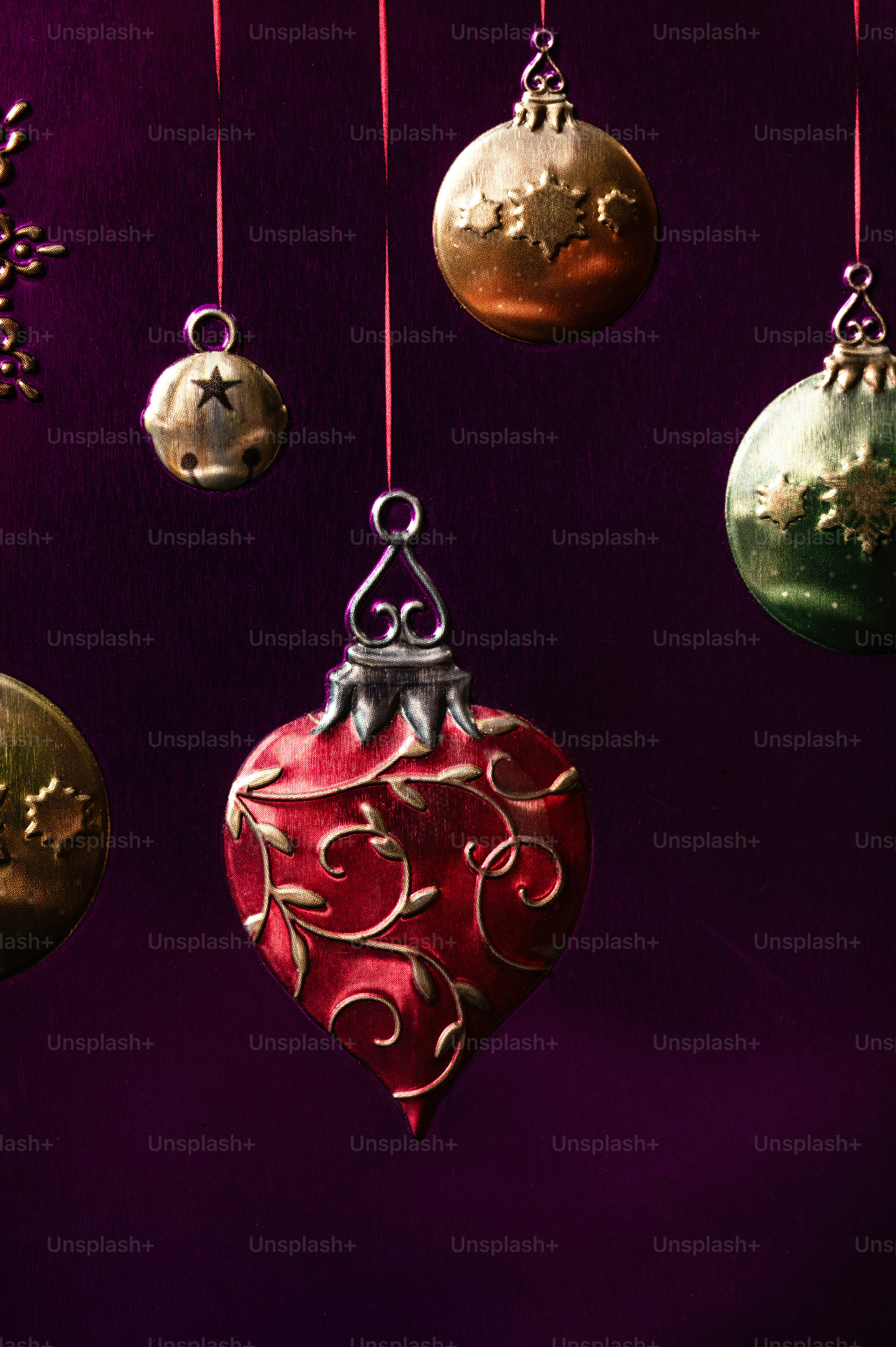 Red heart-shaped and round metallic Christmas ornaments hanging against a dark purple background