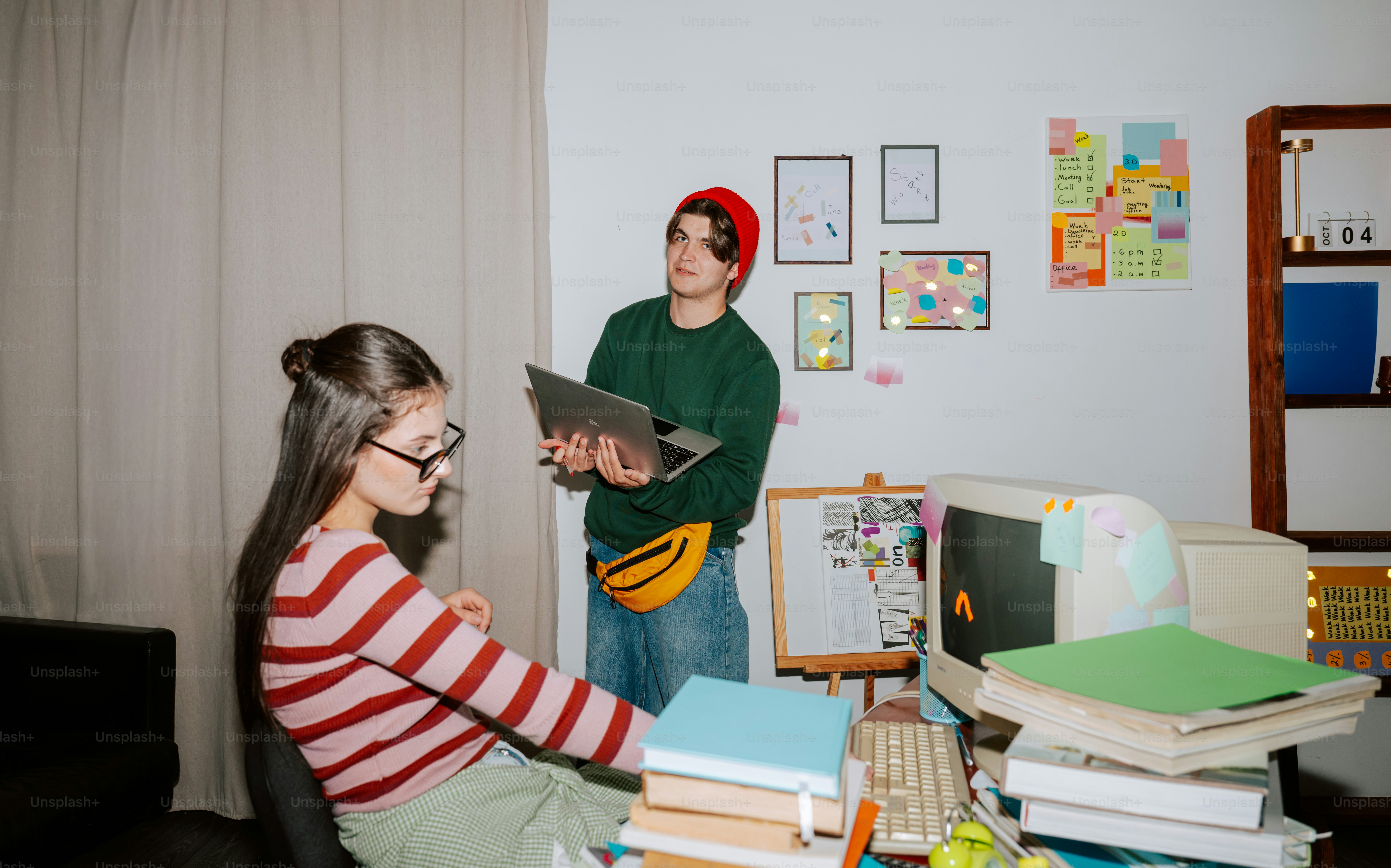 A woman sitting at a desk and a man holding a laptop in a workspace