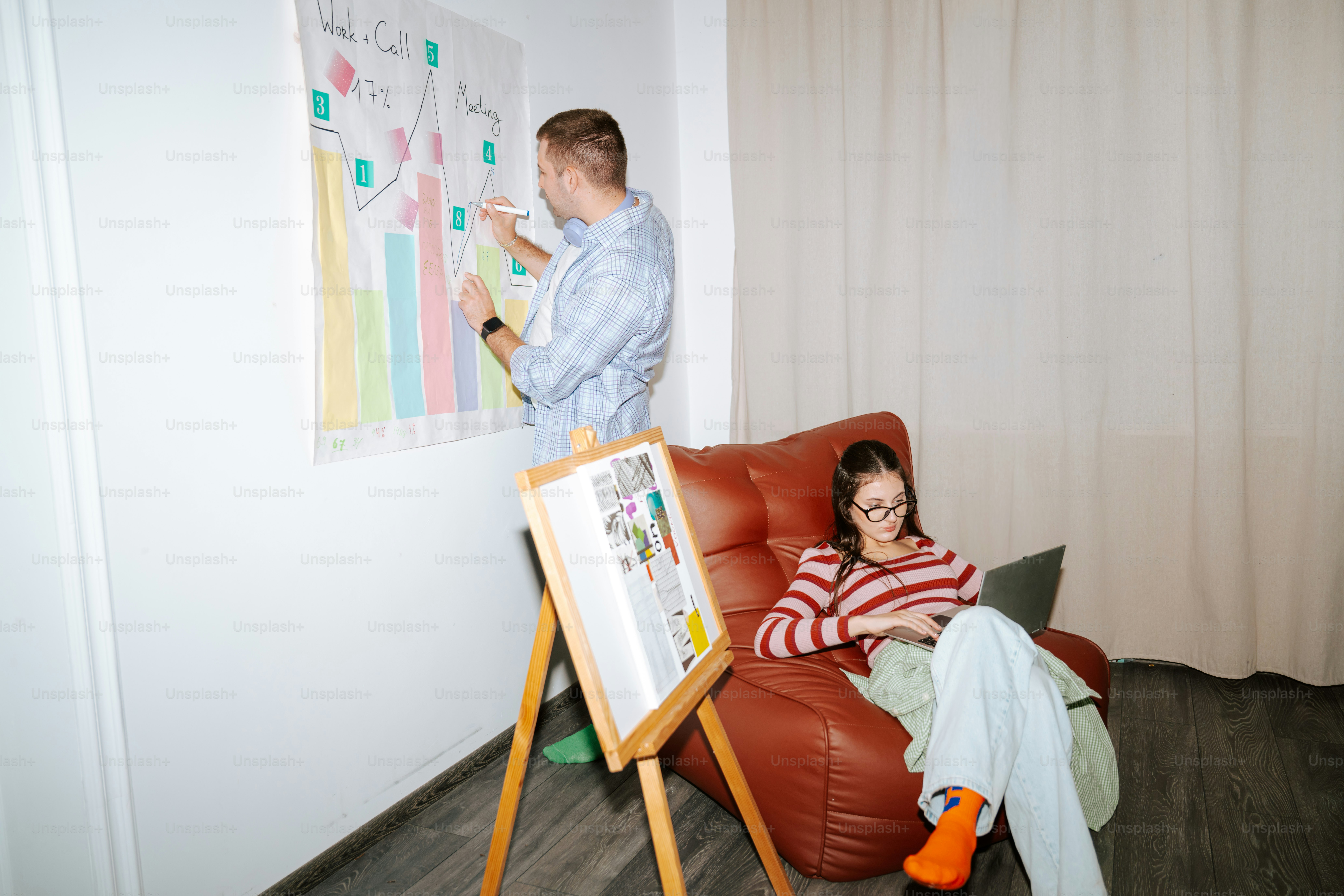 A man writing on a wall chart while a woman uses a laptop nearby