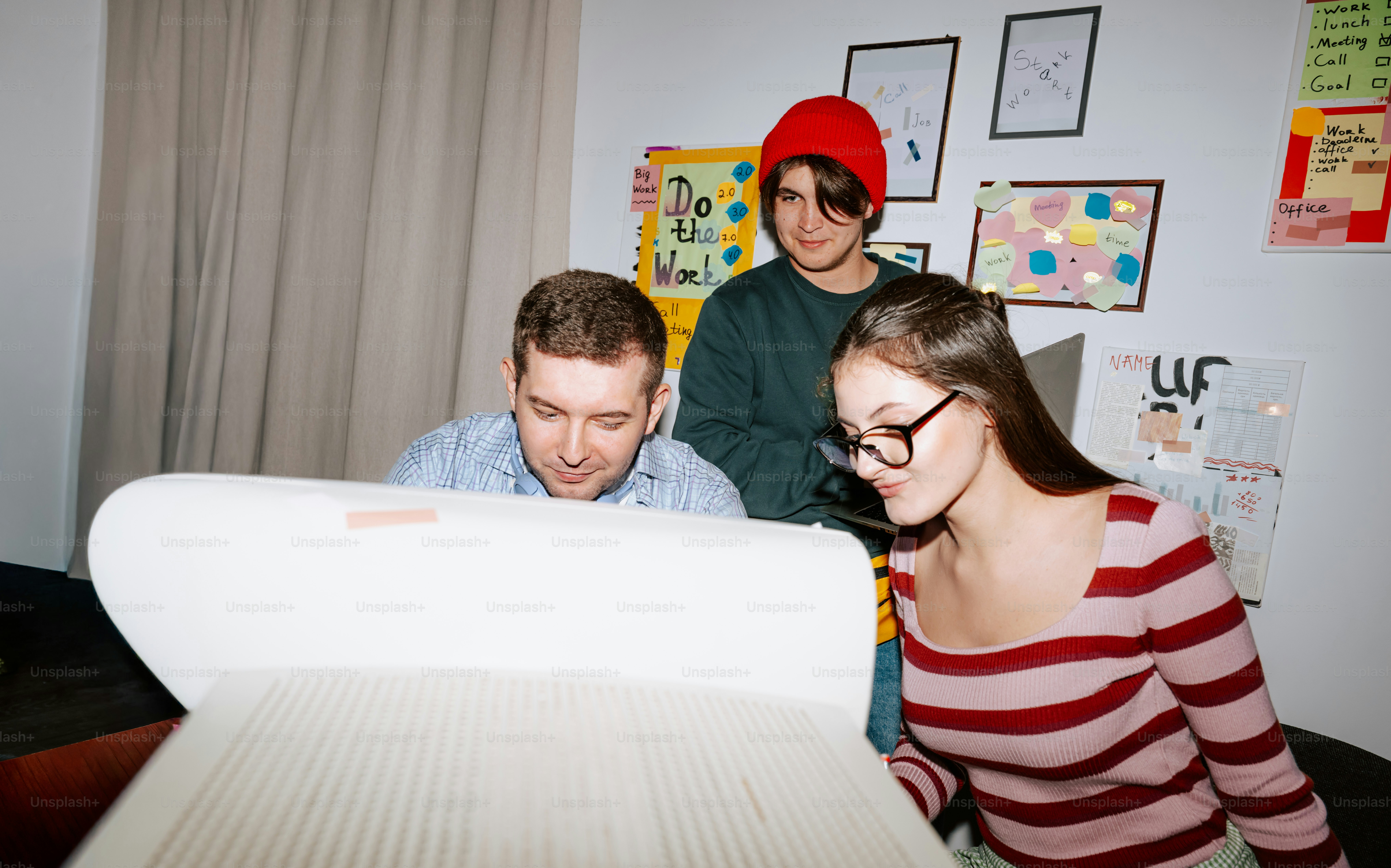 Three people looking at a document in a workspace with notes on the wall