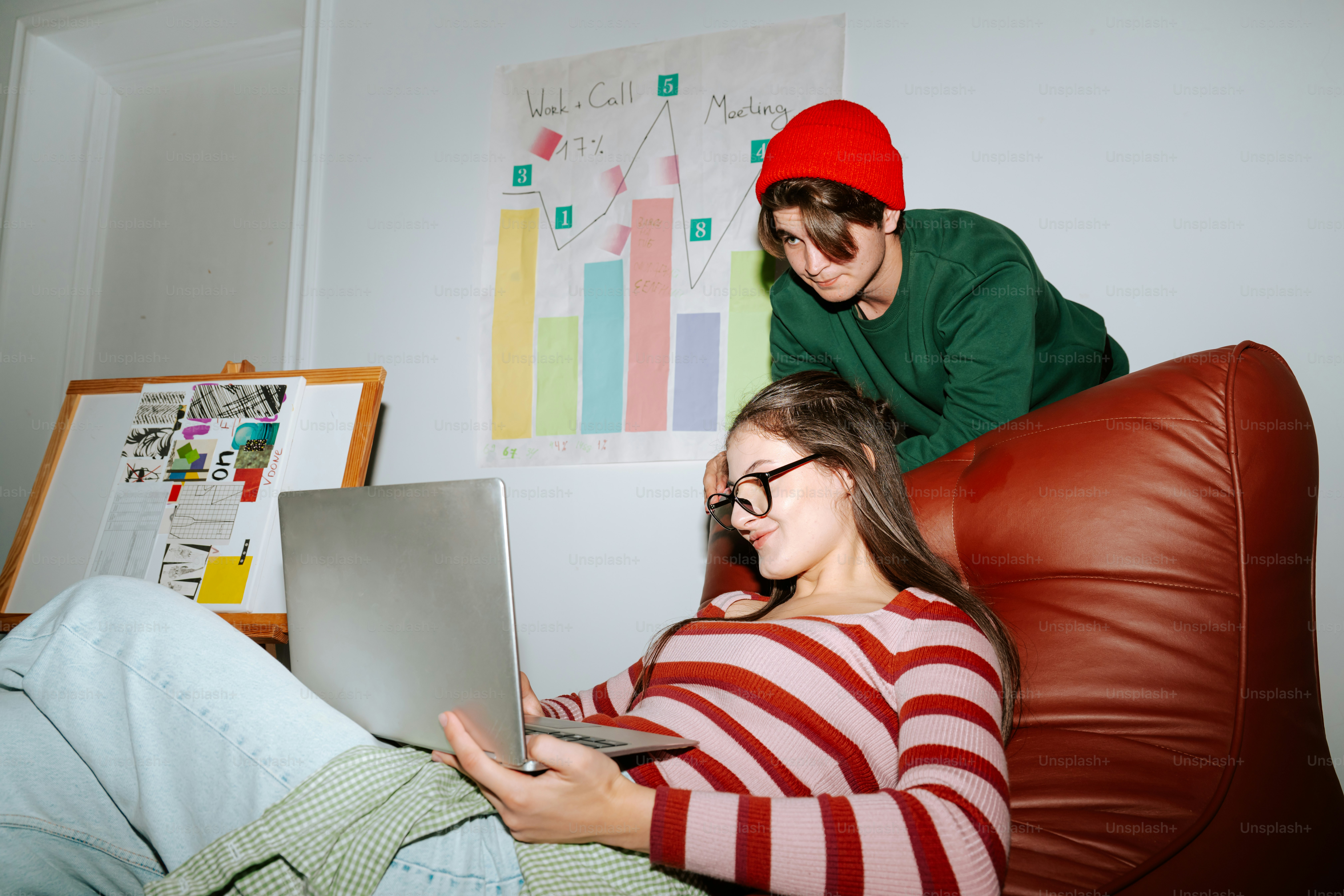 A woman in a striped shirt using a laptop while a man watches