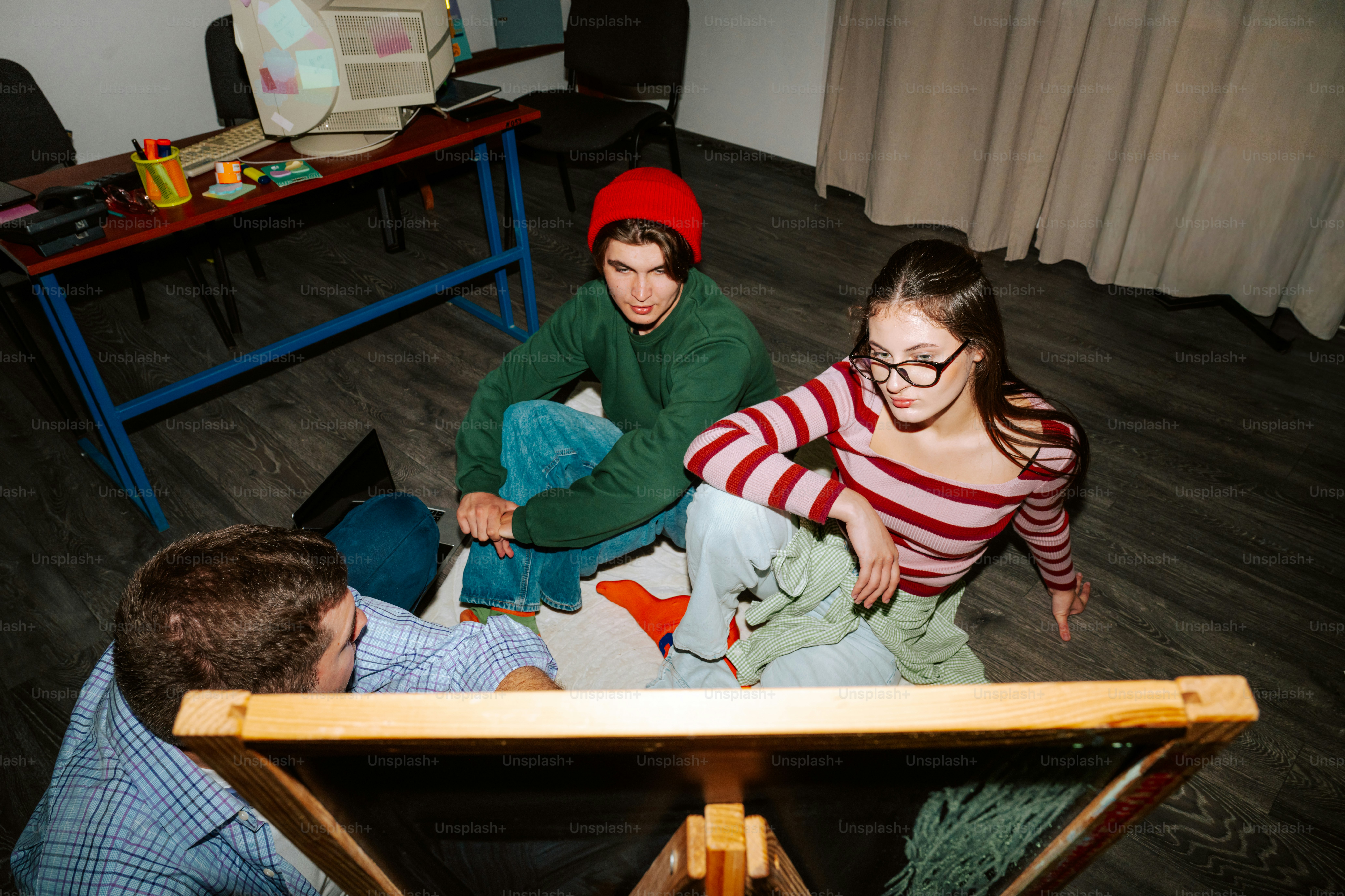 Three people sitting on the floor in a room with a wooden easel
