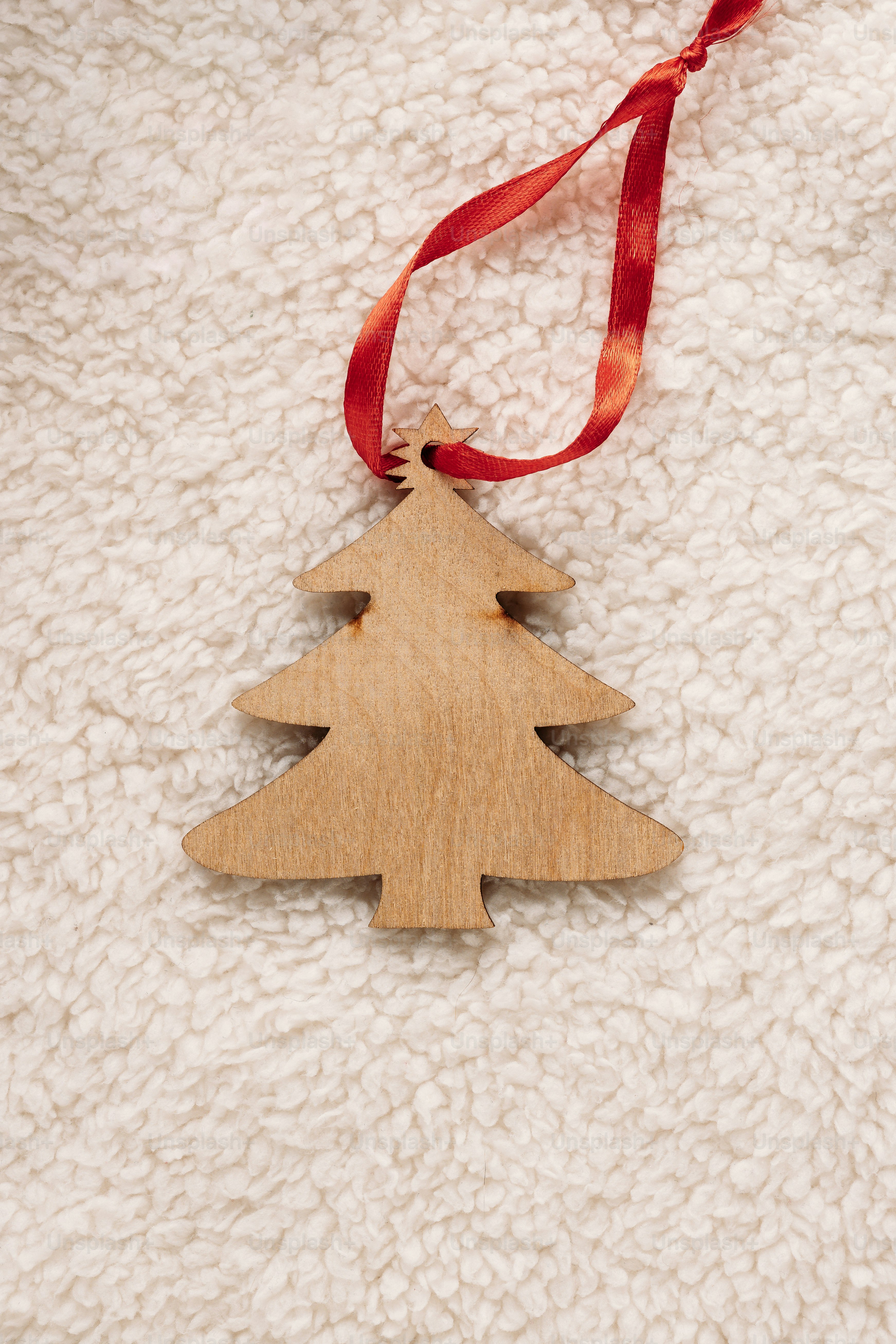 A wooden Christmas tree ornament with a red ribbon on white faux fur
