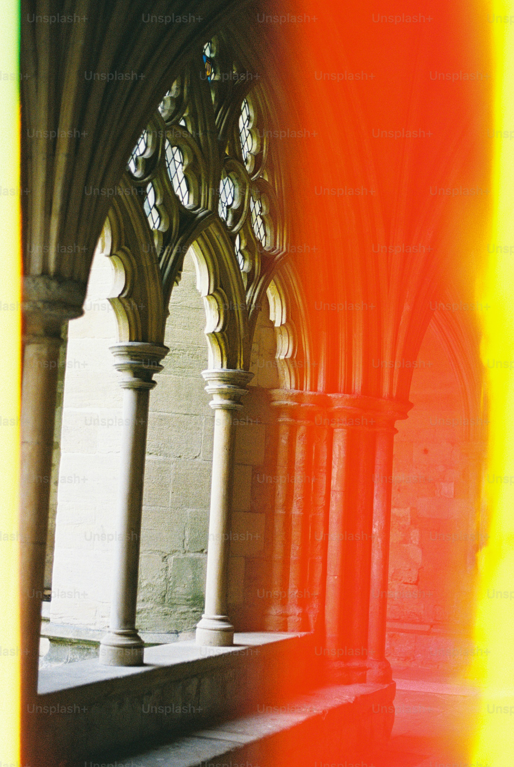 Arcos y columnas de piedra en un claustro con filtraciones de luz roja y amarilla brillante