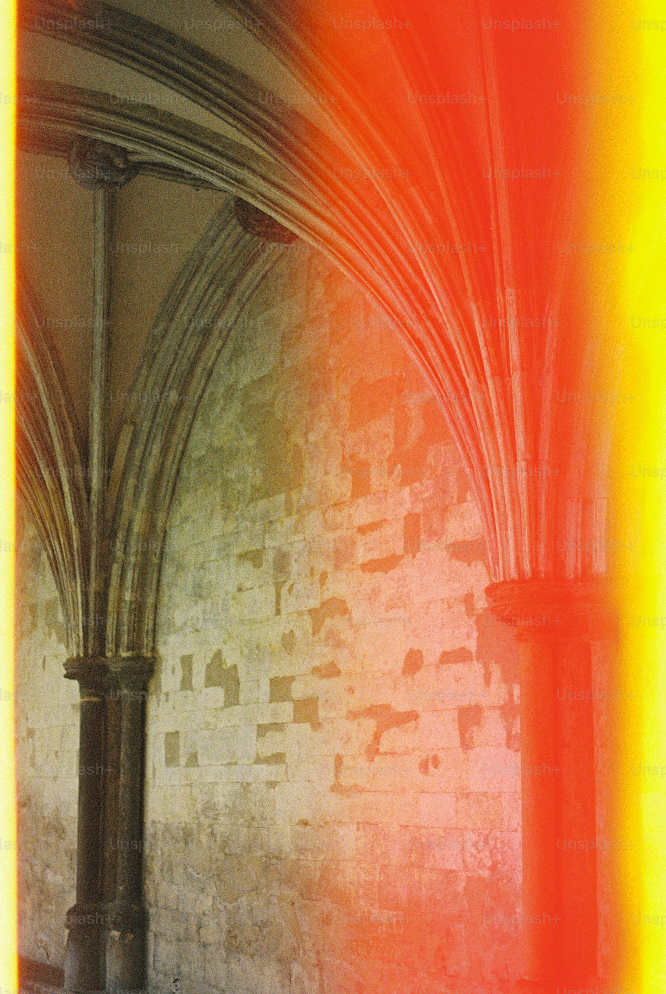 Stone columns and vaulted arches against a textured wall with bright orange light leaks