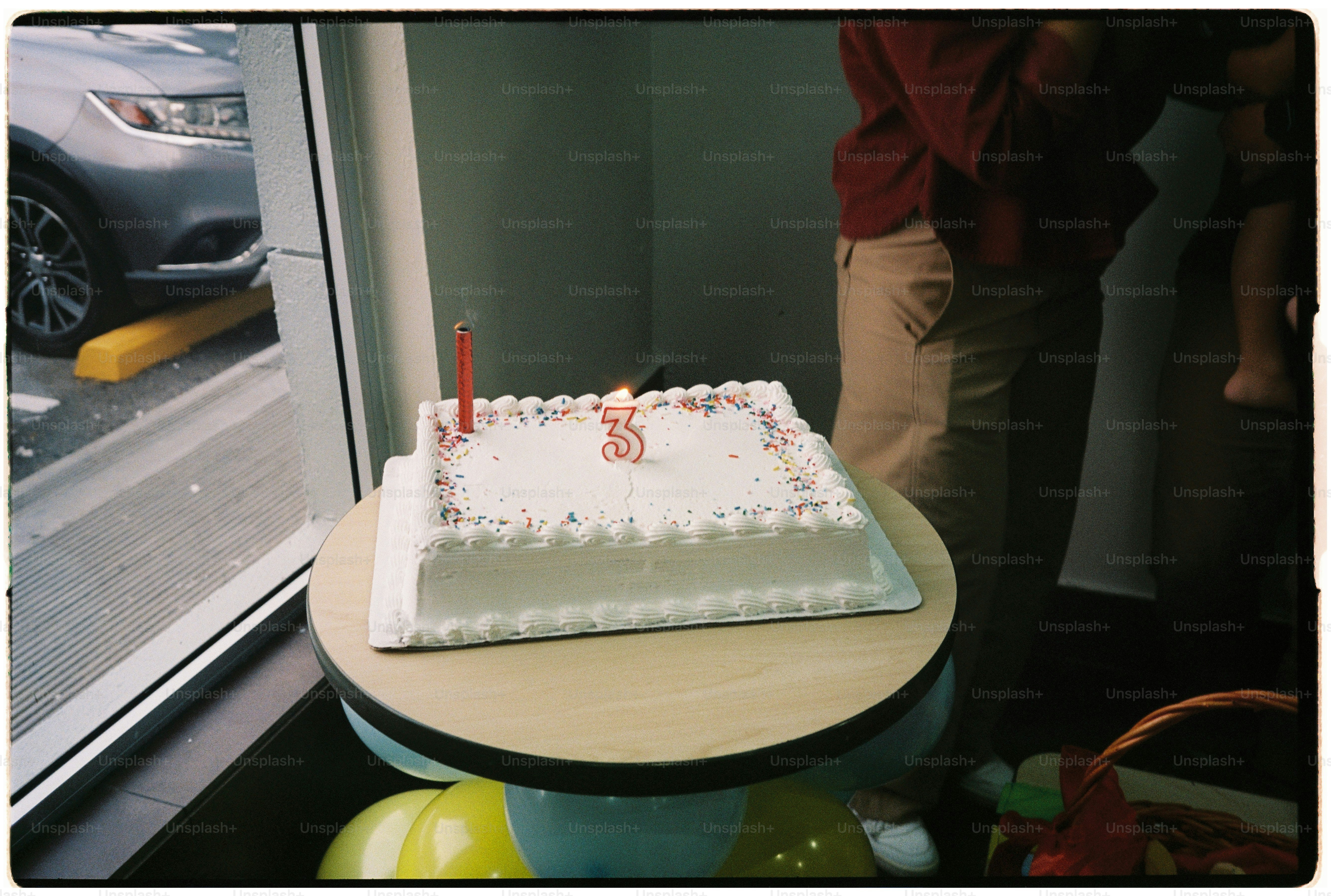 A rectangular white birthday cake with sprinkles and a number three candle on a table