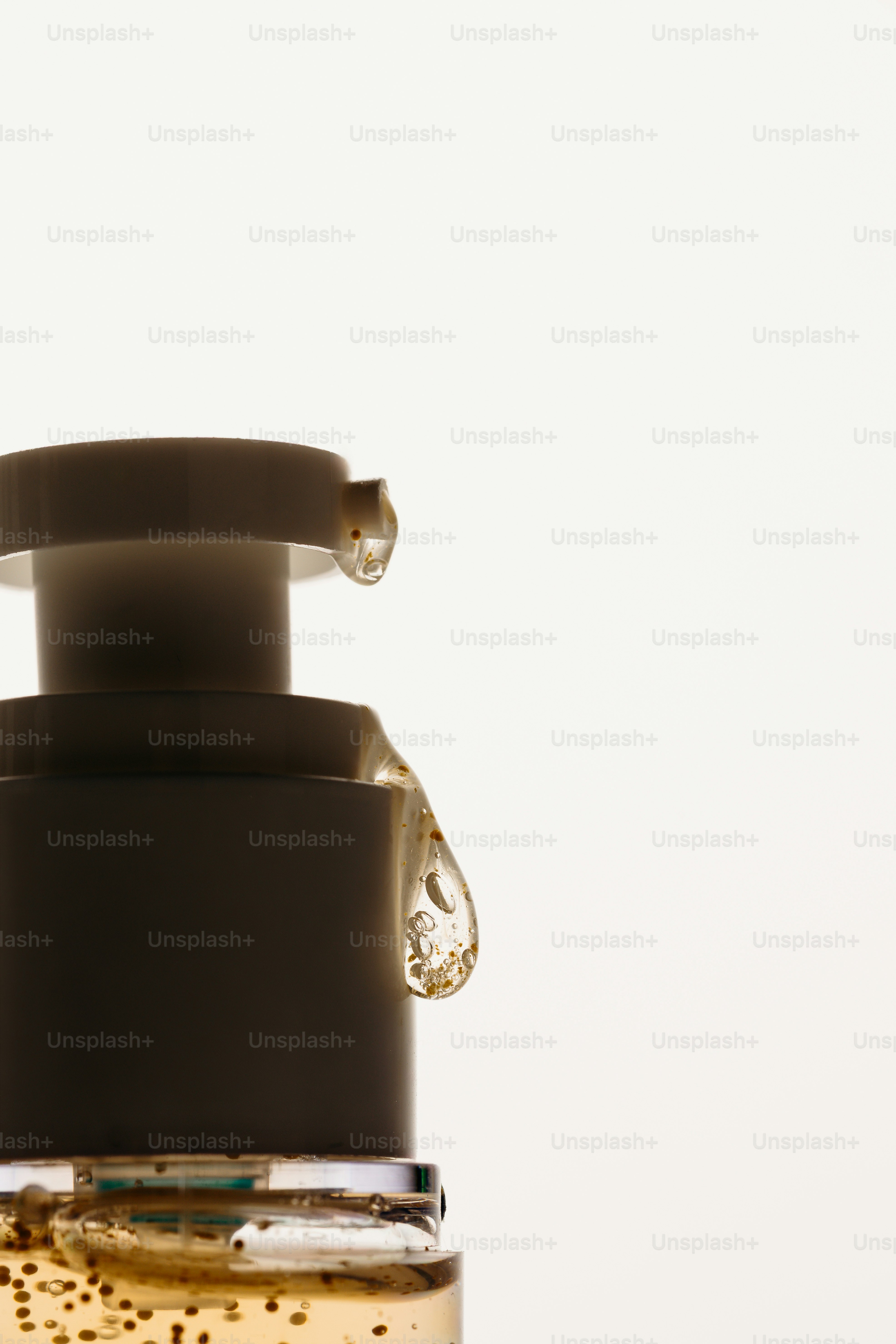 A drop of golden serum clinging to the nozzle of a white pump bottle