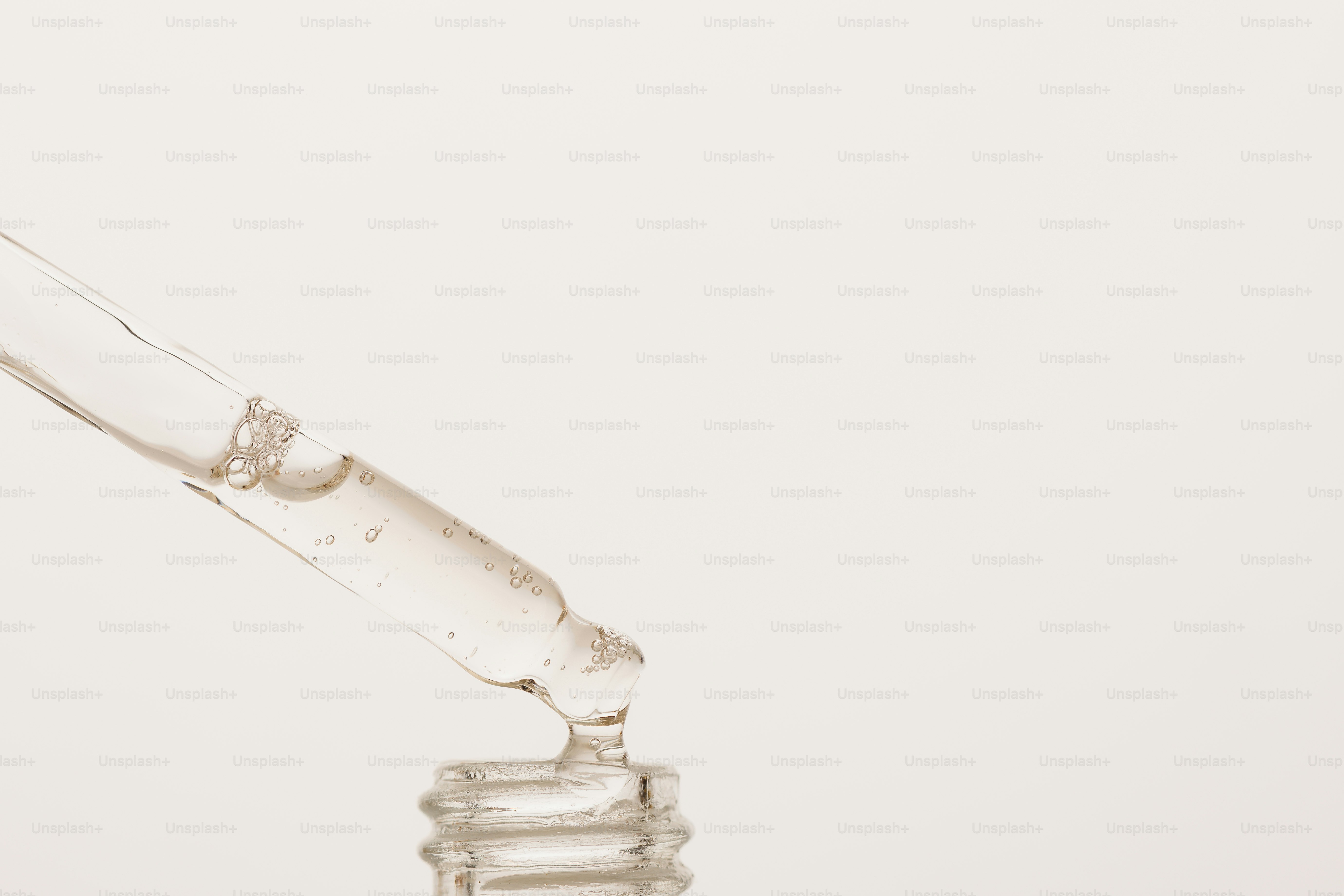 A glass dropper dispensing a clear liquid into a bottle against a beige background