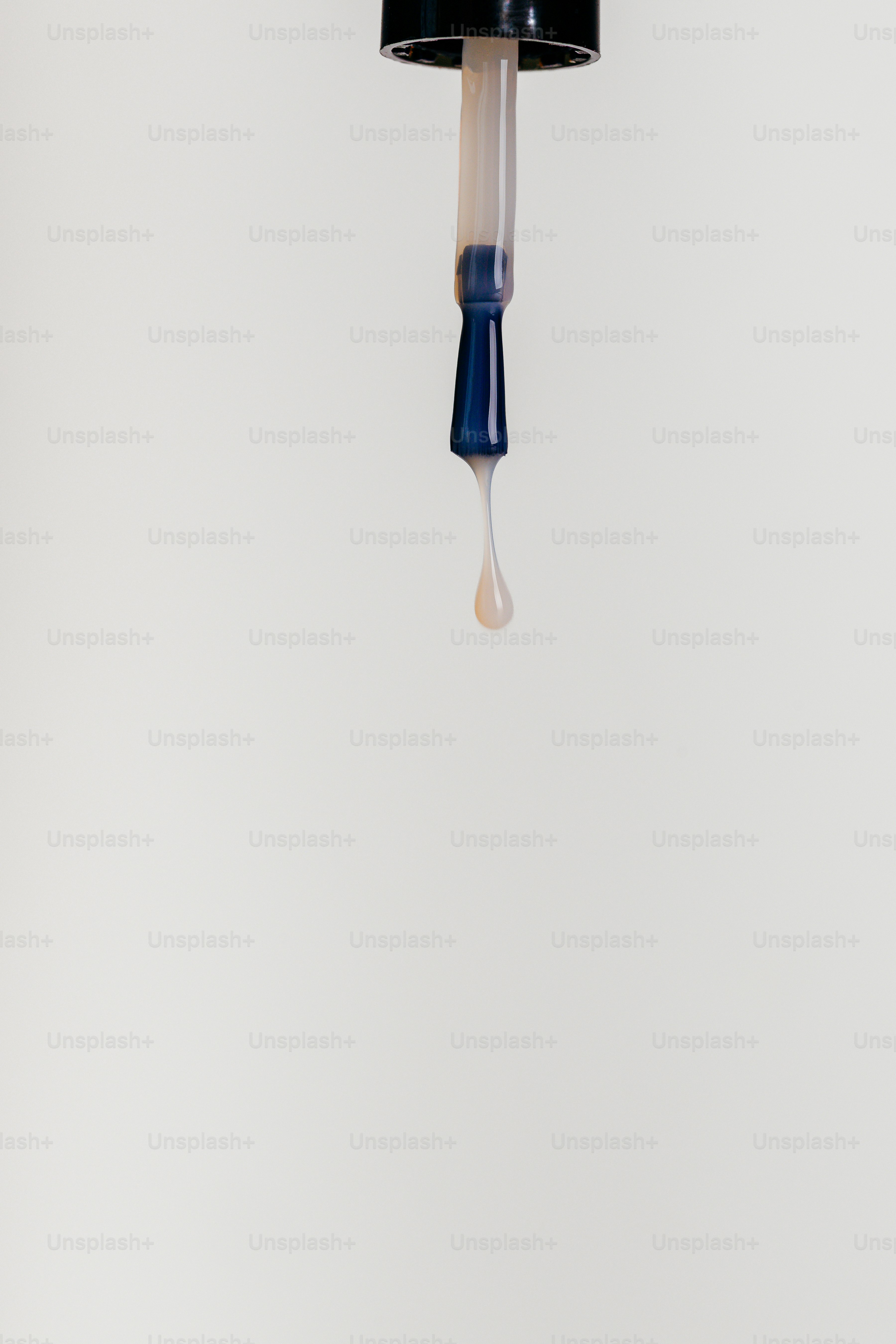 A nail polish brush dripping a clear liquid against a plain light background