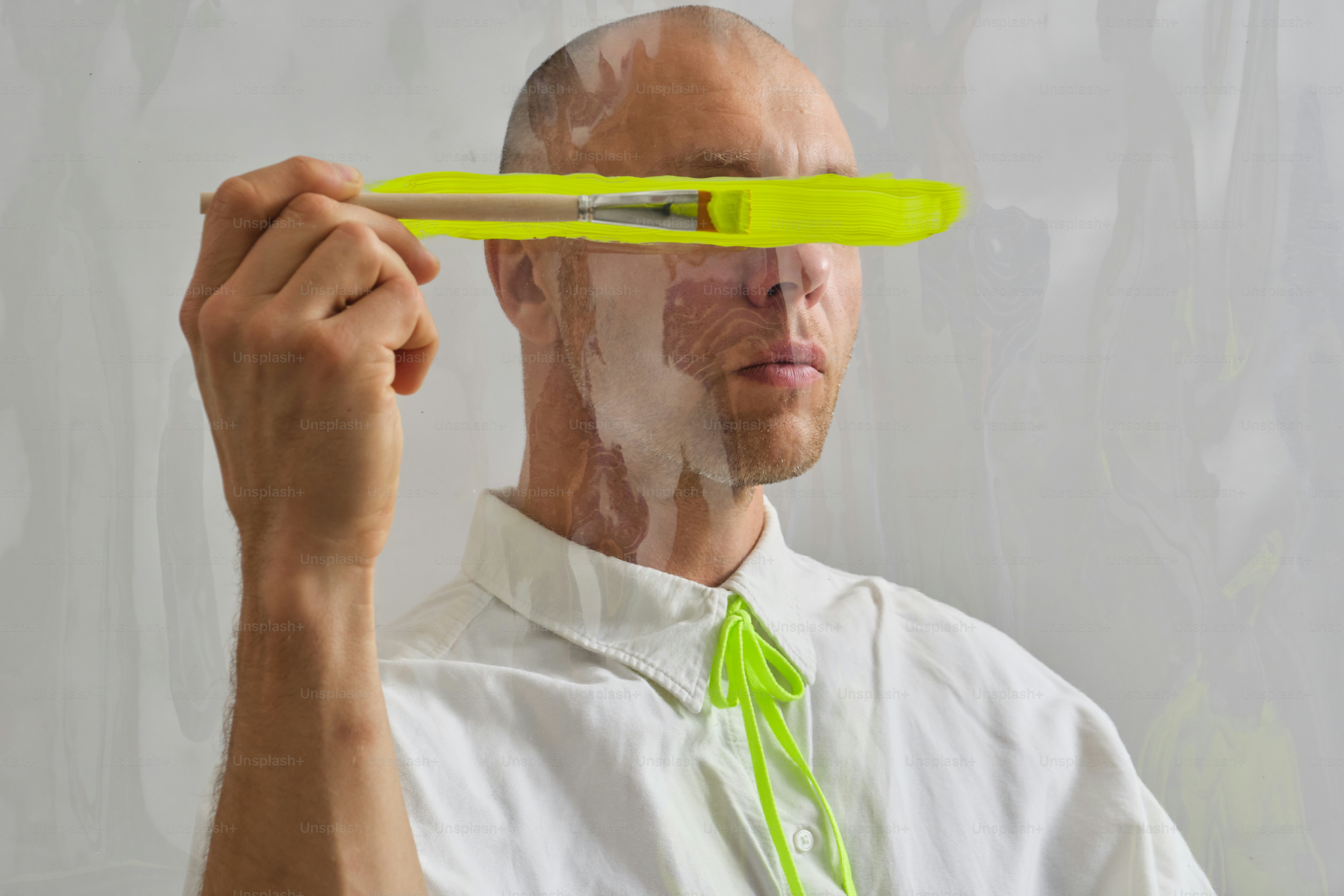電気イエローの絵具を目に塗った筆を持つ男