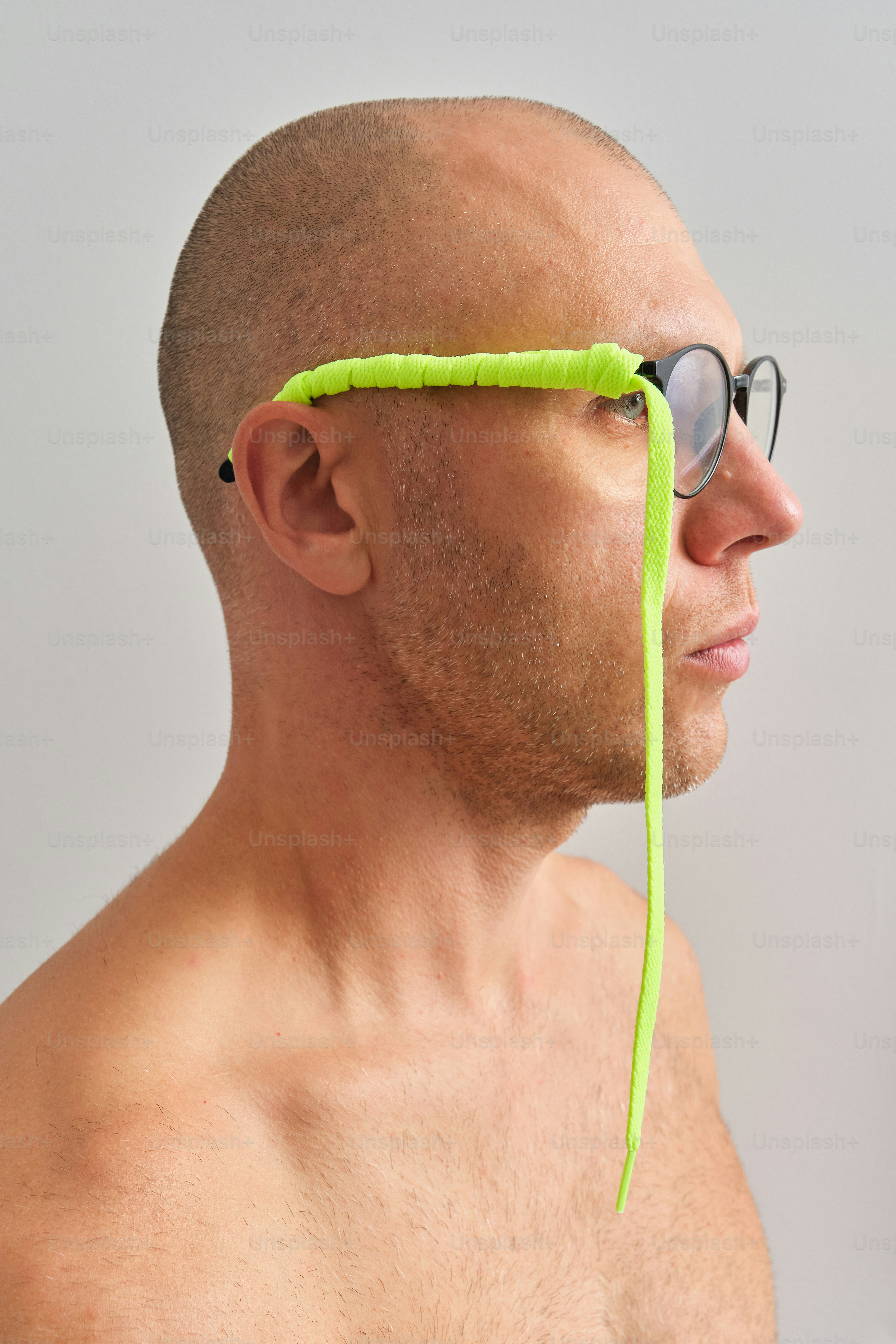 眼鏡をかけ、明るい電気黄色の靴ひもをフレームに巻きつけた男