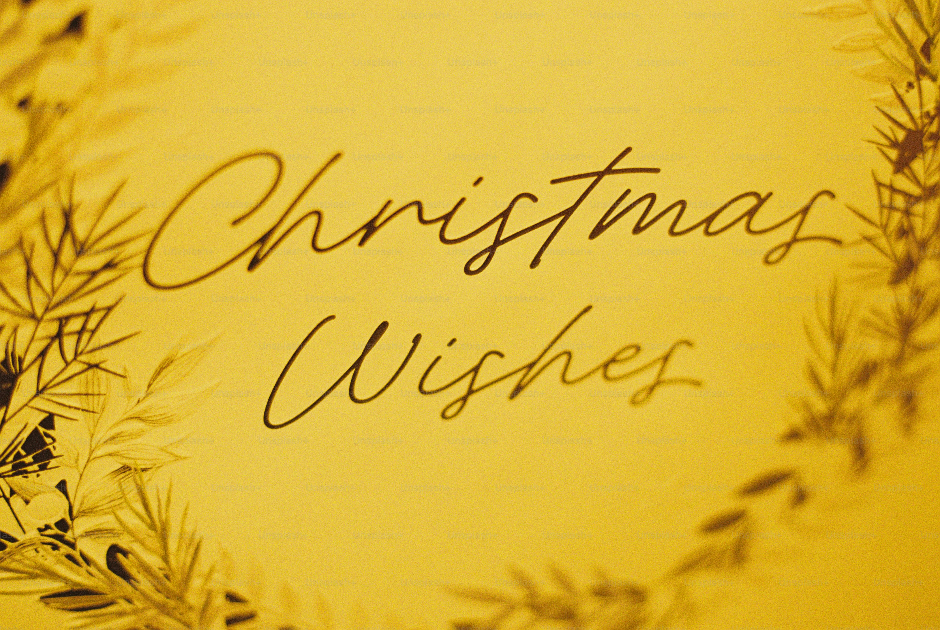 Festive script reading "Christmas Wishes" in dark brown on a warm golden yellow background with blurred foliage