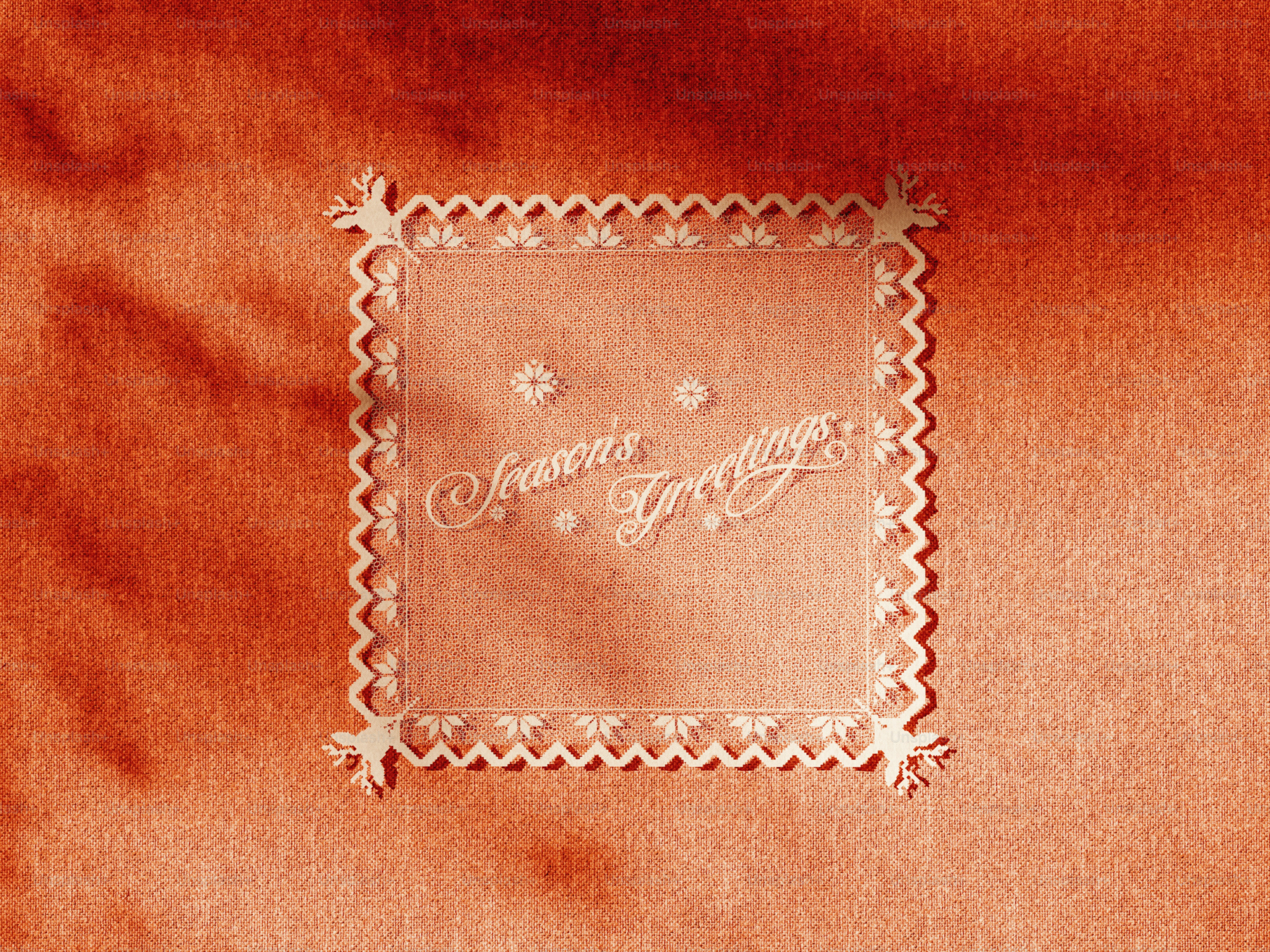 A square lace frame with reindeer corners and the text Season's Greetings on orange fabric