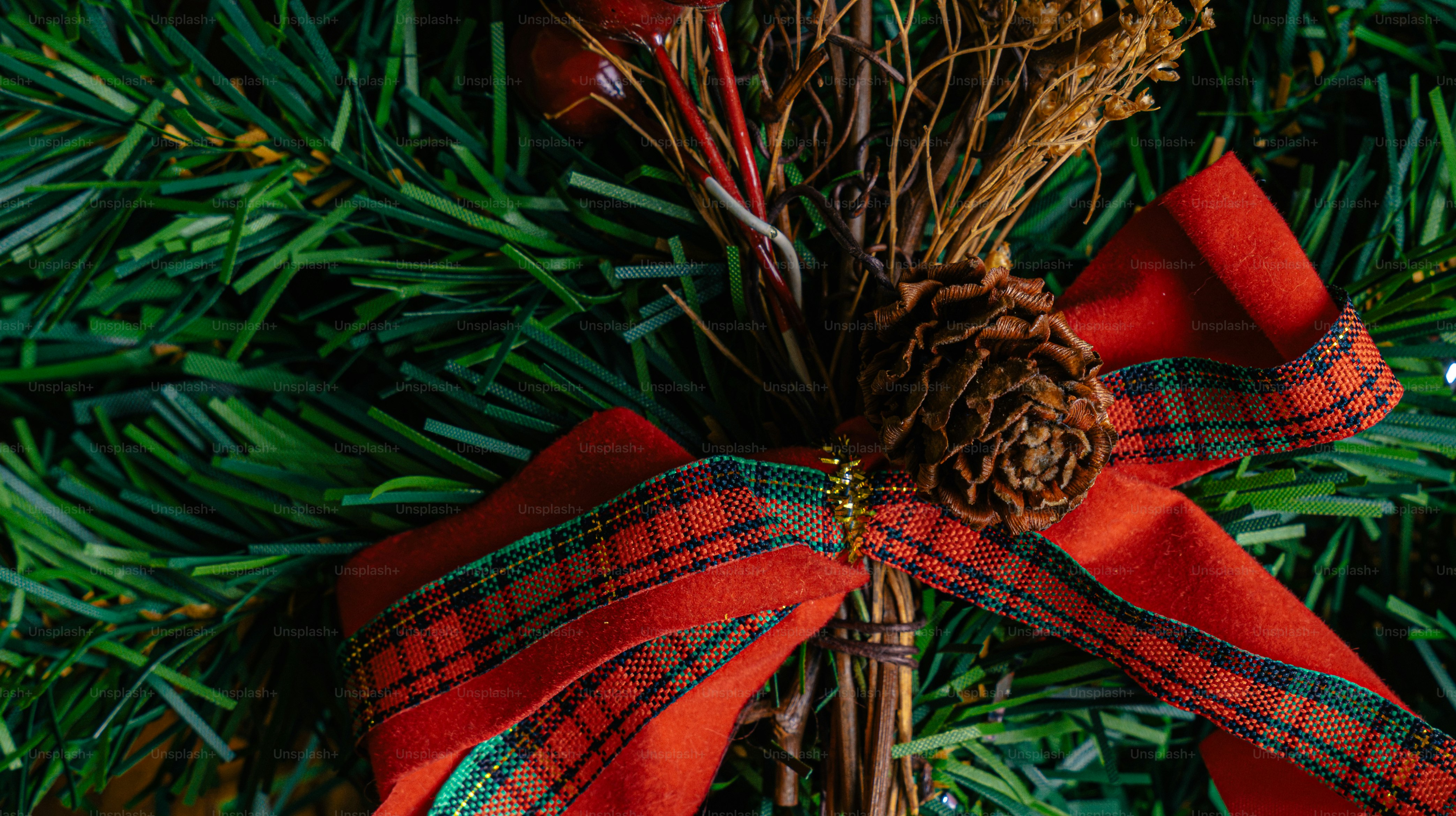 A pine cone and red velvet ribbon on a green artificial wreath