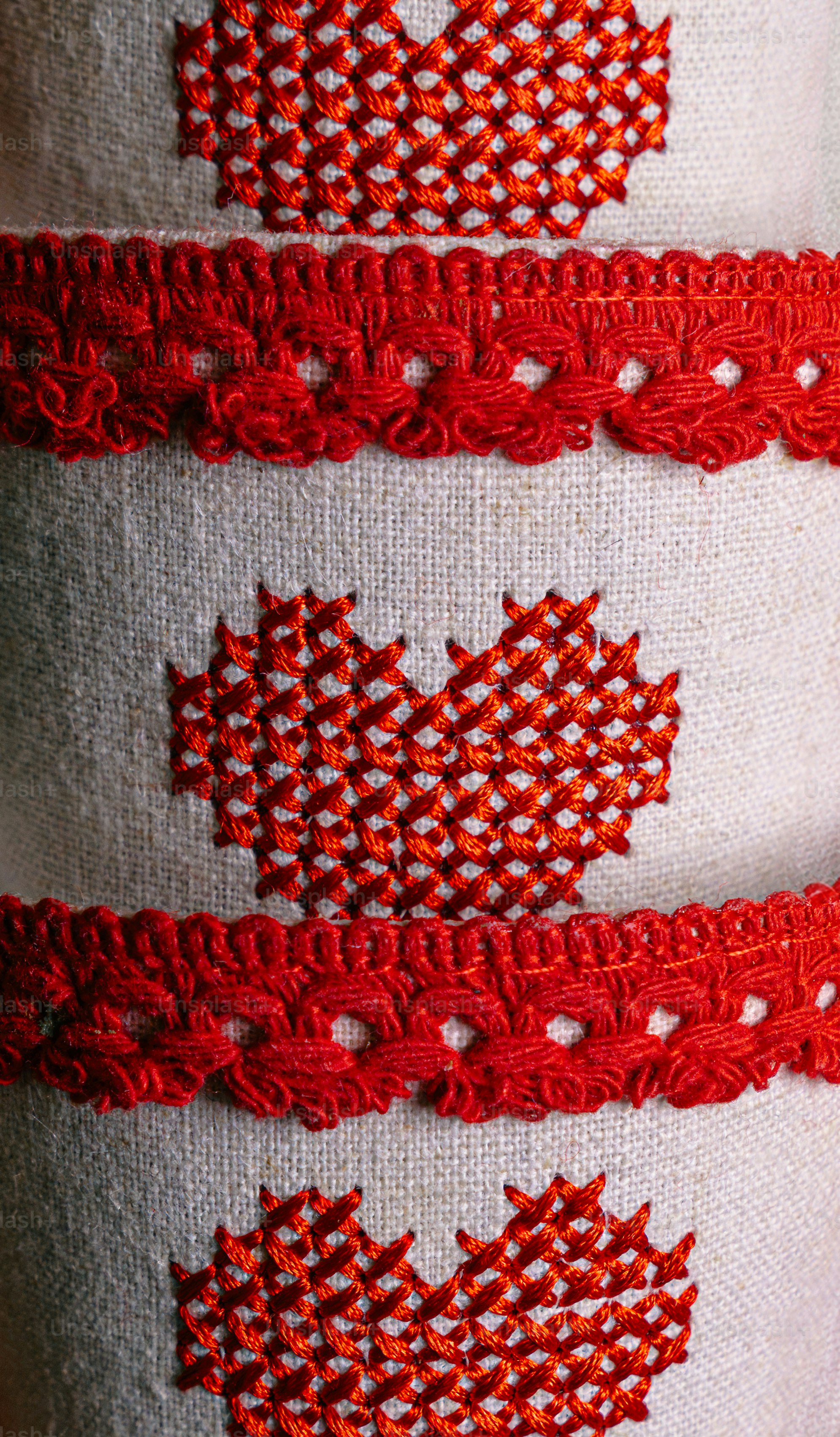 Red cross-stitch hearts and decorative lace trim on a beige linen fabric