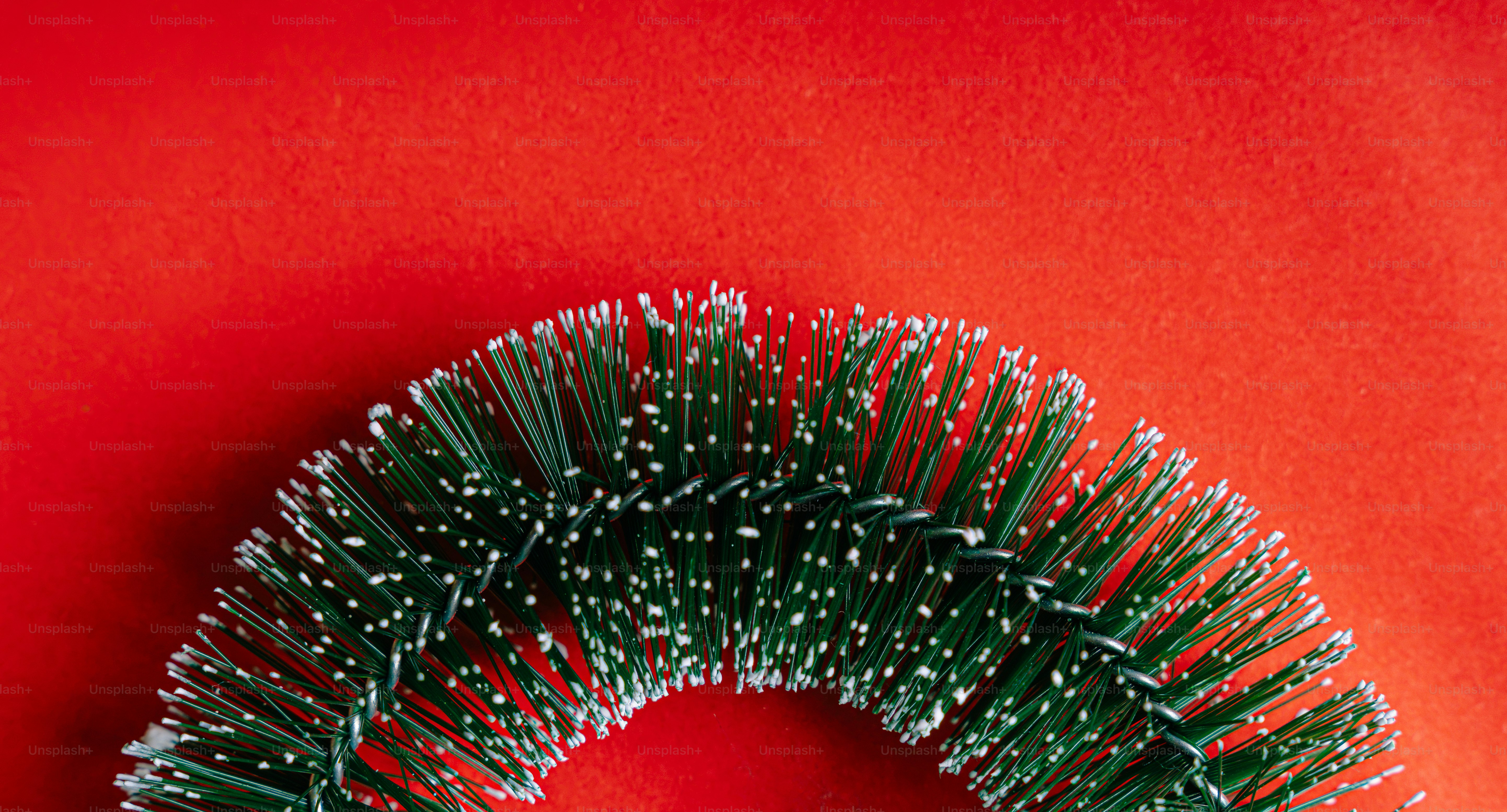 A curved section of a green artificial pine garland with white tips on red