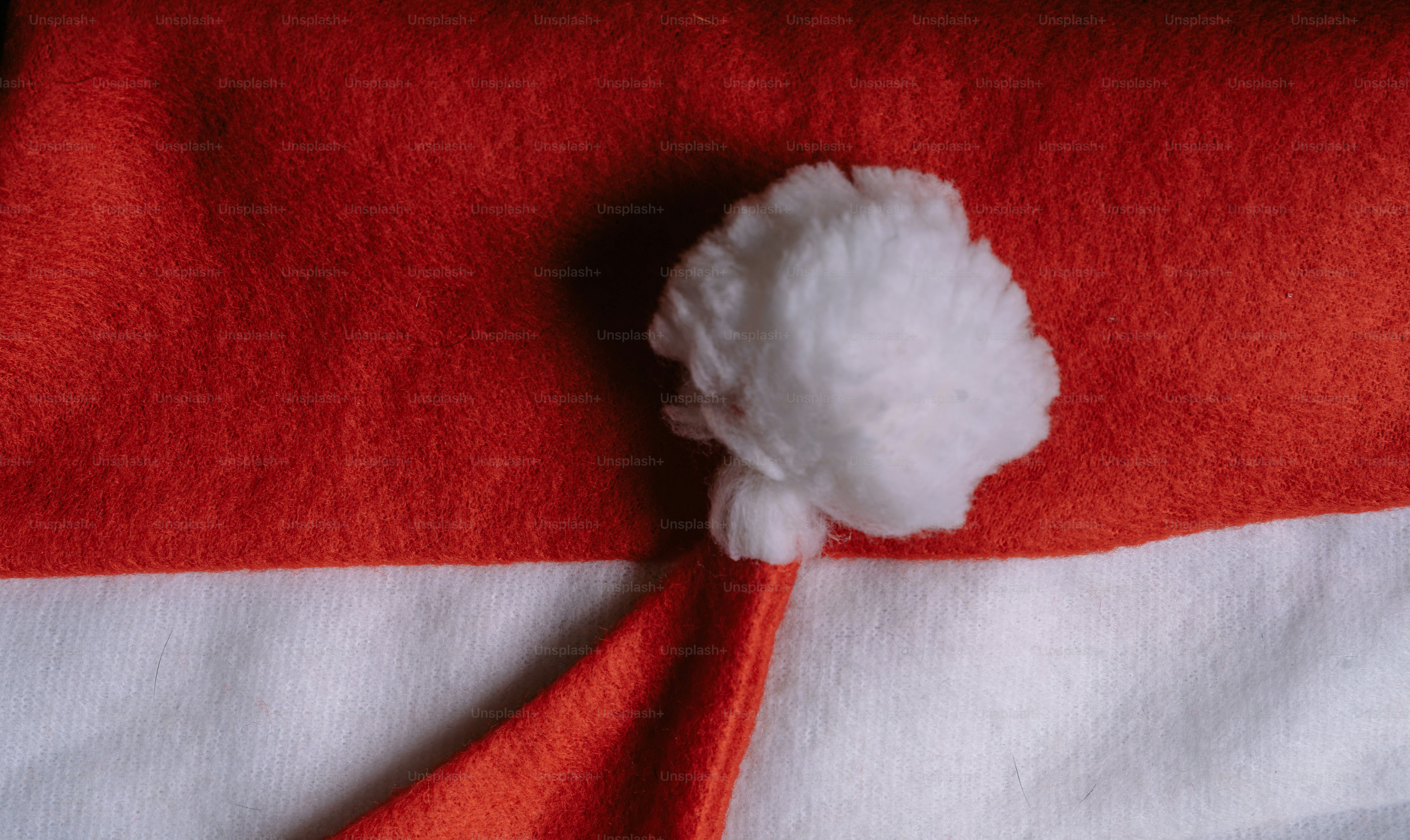A red felt Santa hat with a white pom-pom on a white fabric